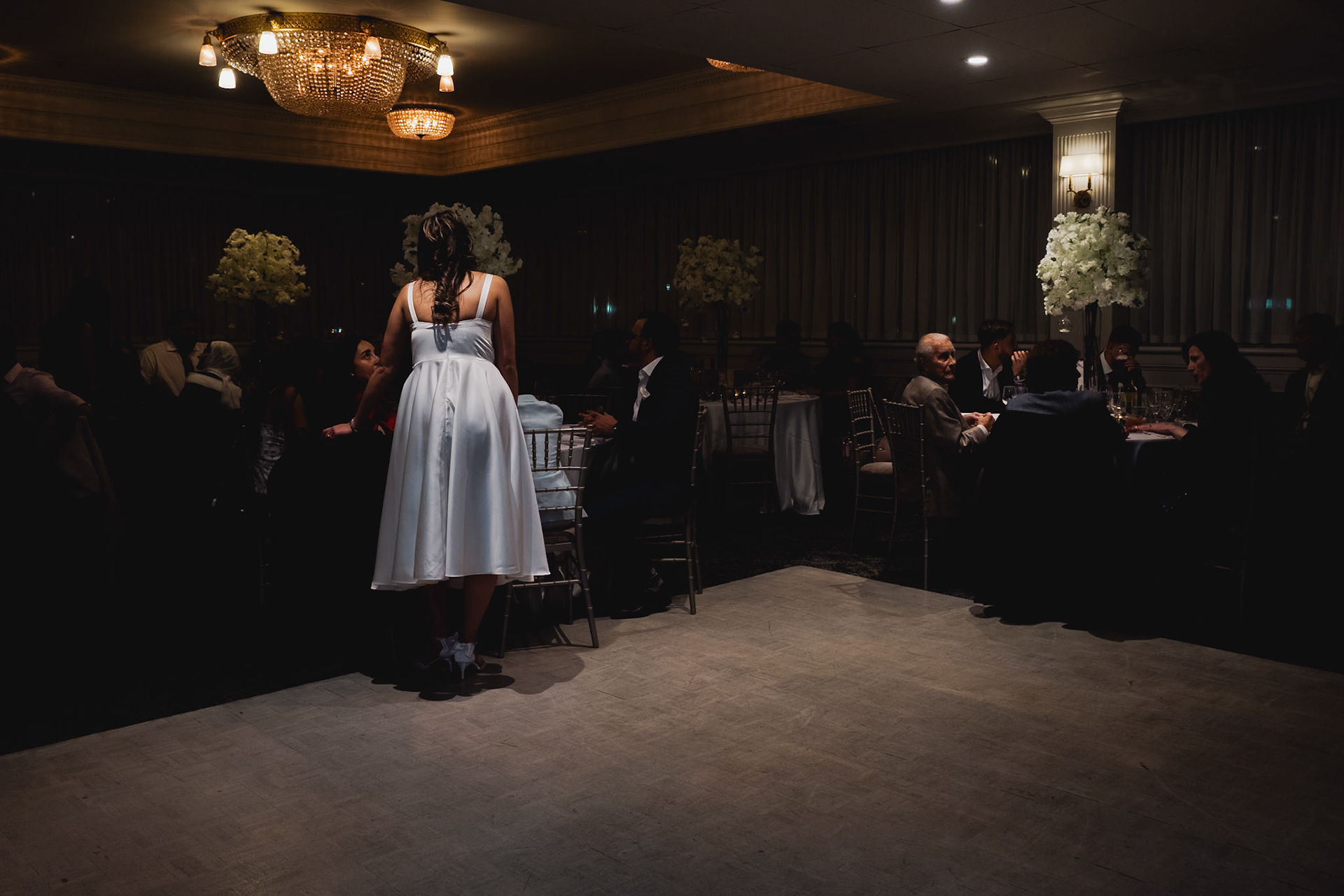 Bride in white dress delivering a speech on a spotlighted dance floor during engagement celebration in Toronto