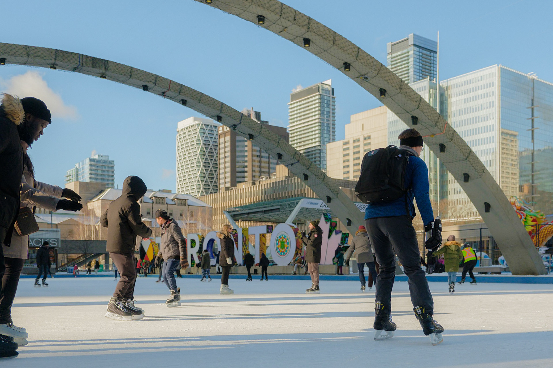People ice skating at Nathan Phillips Square under the Toronto sign during winter, street candid by Cristian Arango