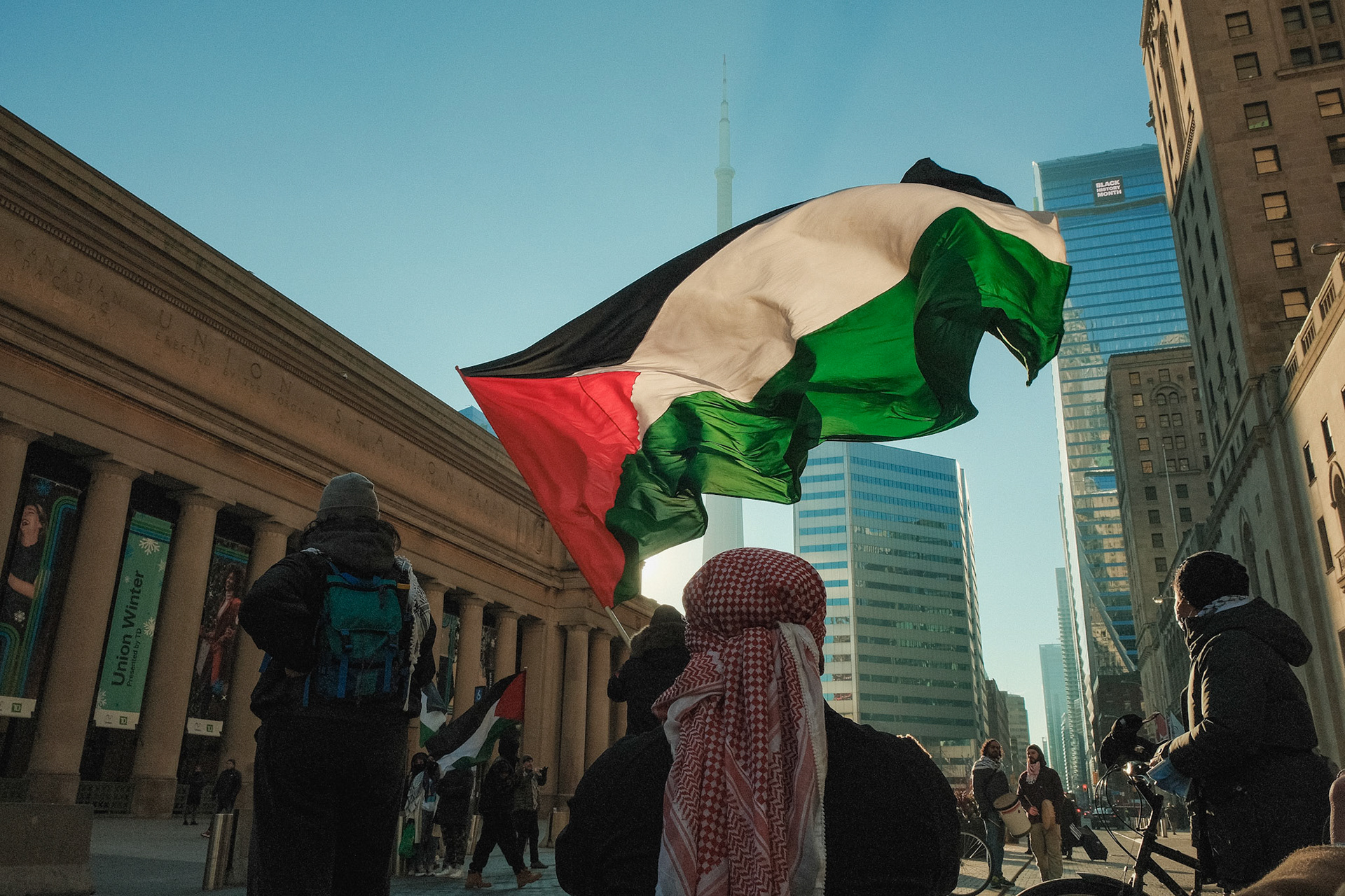 Pro-Palestine flag raised high during a demonstration in Toronto, symbolizing solidarity and resistance against the ongoing Israel-Palestine conflict. Political street photography.