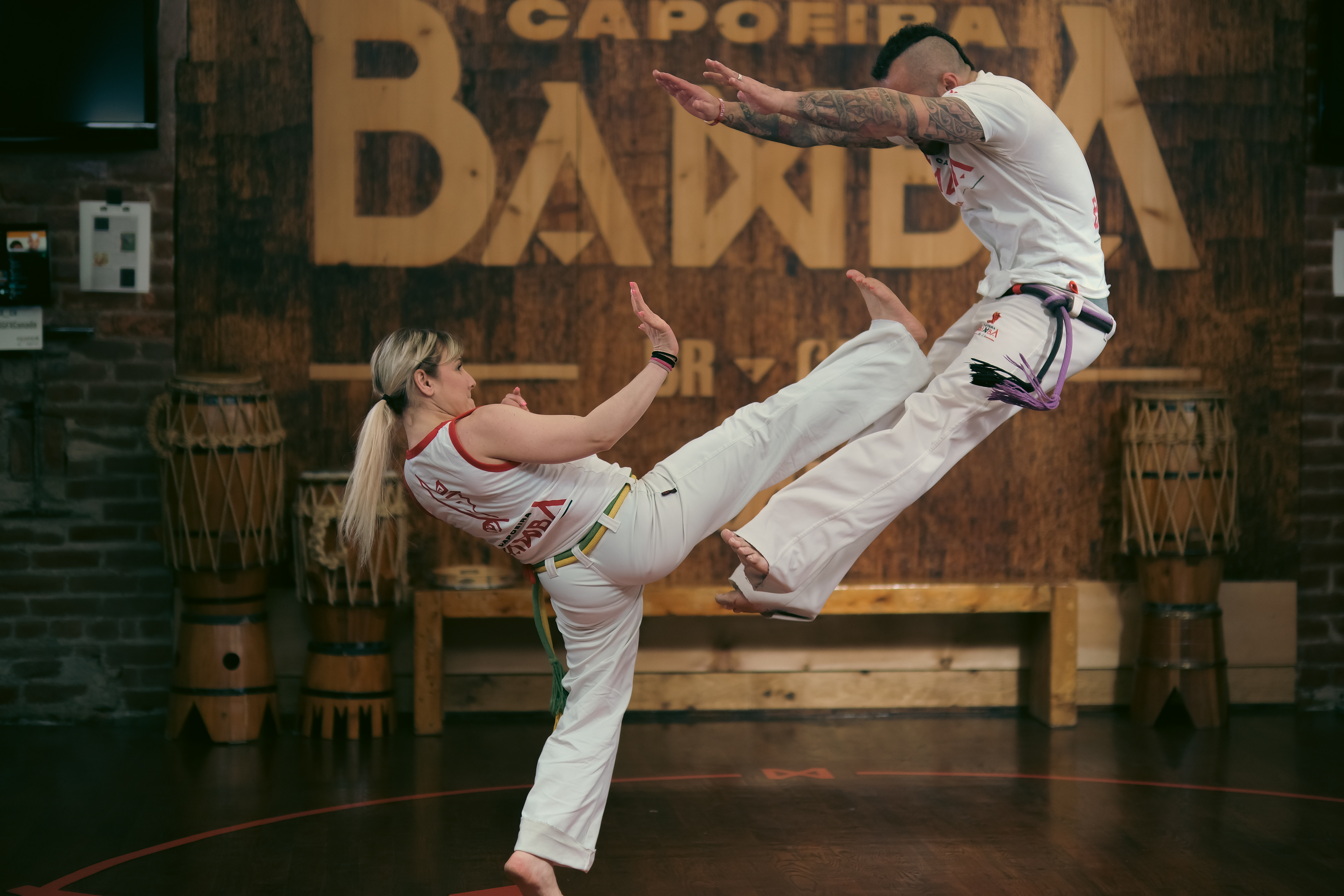 Intense exchange between two Capoeiristas, one delivering a counter kick while the other balances mid-air.