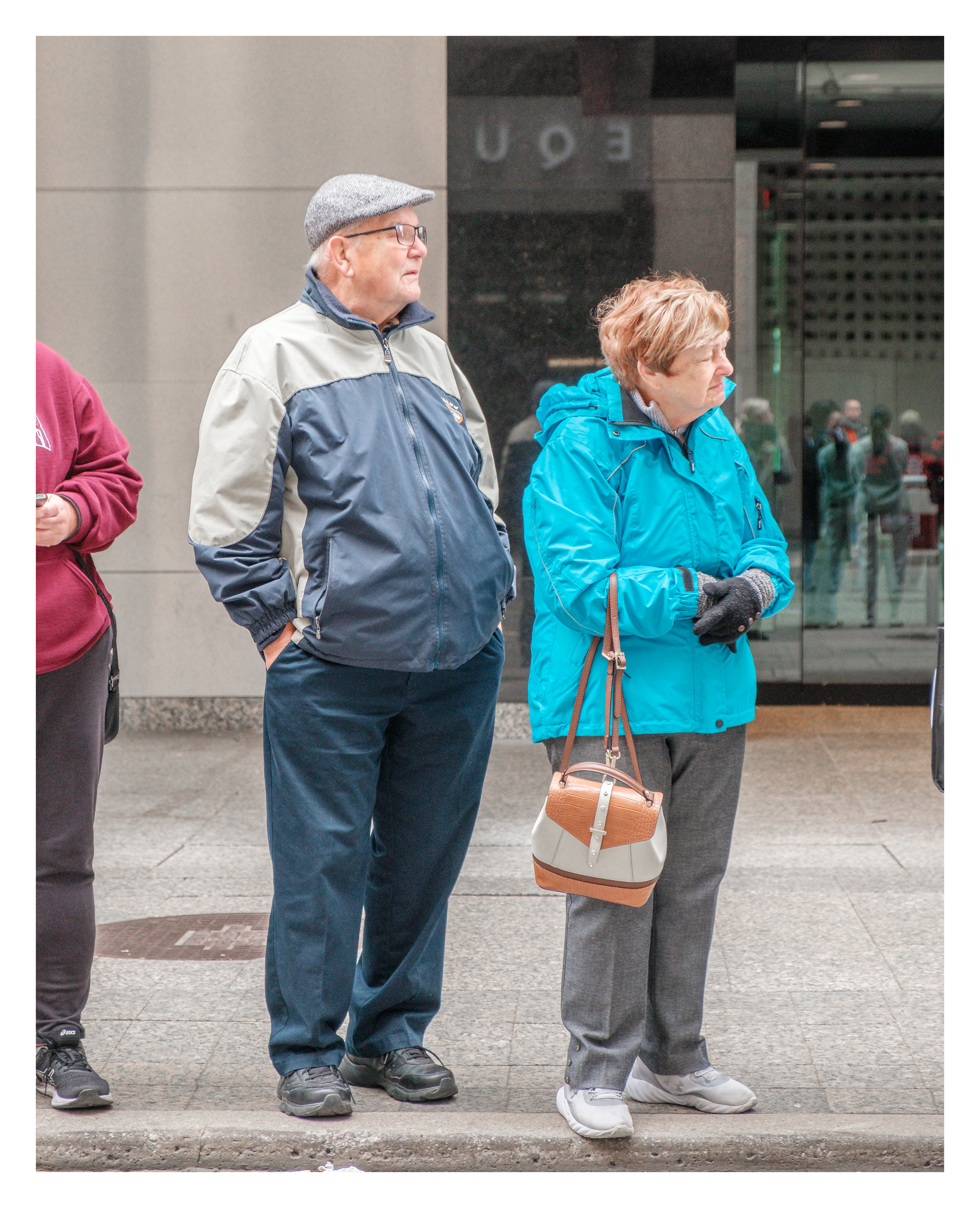 Elderly spectators standing curbside in downtown Toronto, dressed for cold weather and watching the marathon unfold with quiet attention.
