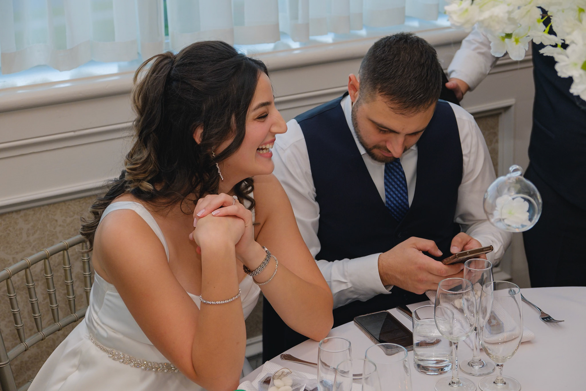 Bride and groom sharing a quiet moment at the dinner table, smiling while checking phone together