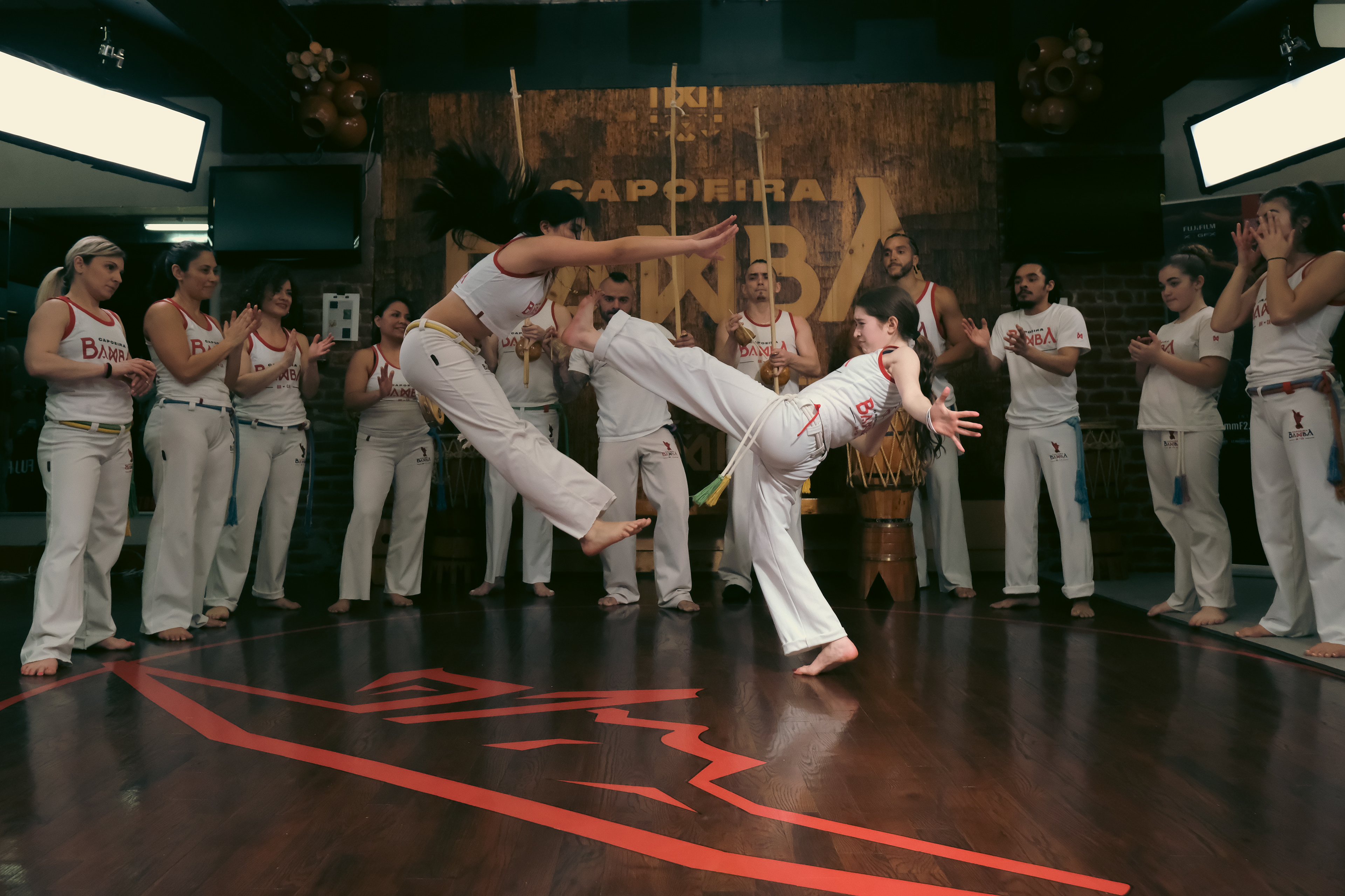 Two Capoeira practitioners exchanging dynamic kicks while surrounded by fellow performers.