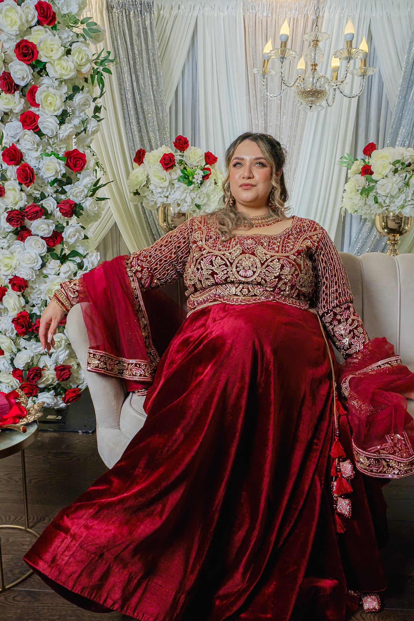 Bride seated alone on floral stage in red velvet lehenga during South Asian engagement in Toronto