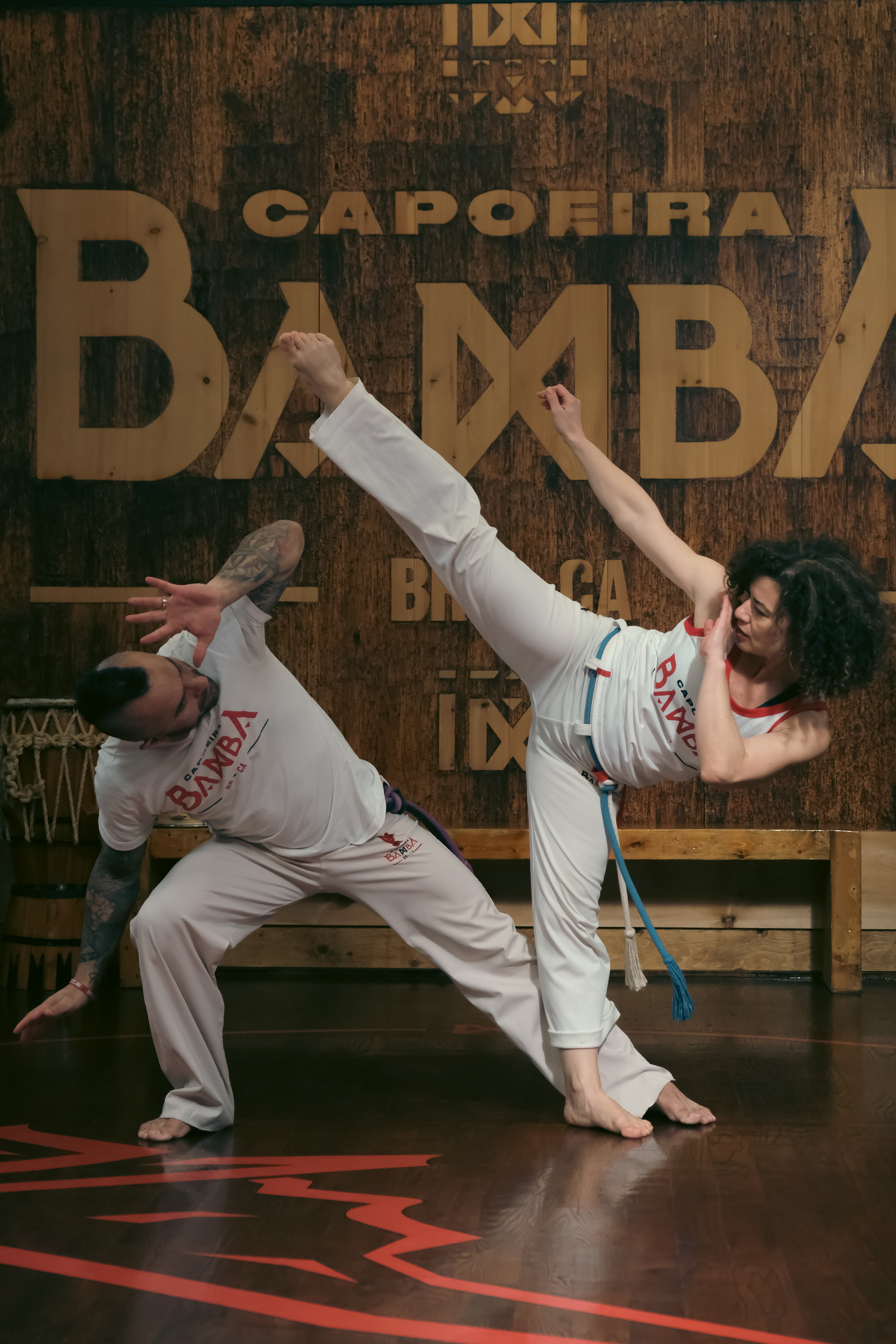 Martial artist mid-kick during a Capoeira roda, legs extended with intensity and control.
