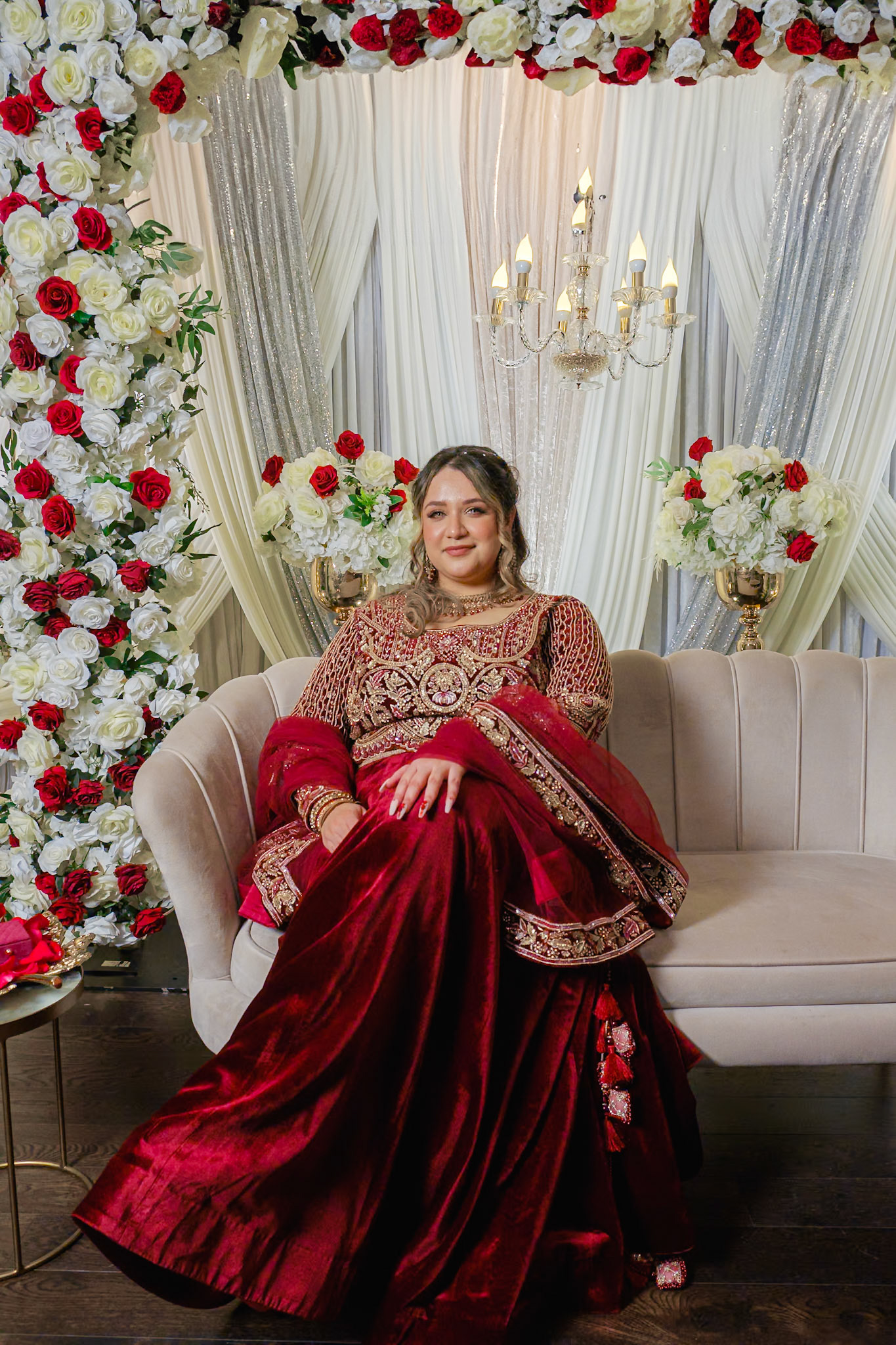 Traditional bride sitting gracefully on stage with red velvet lehenga, captured during Toronto engagement ceremony