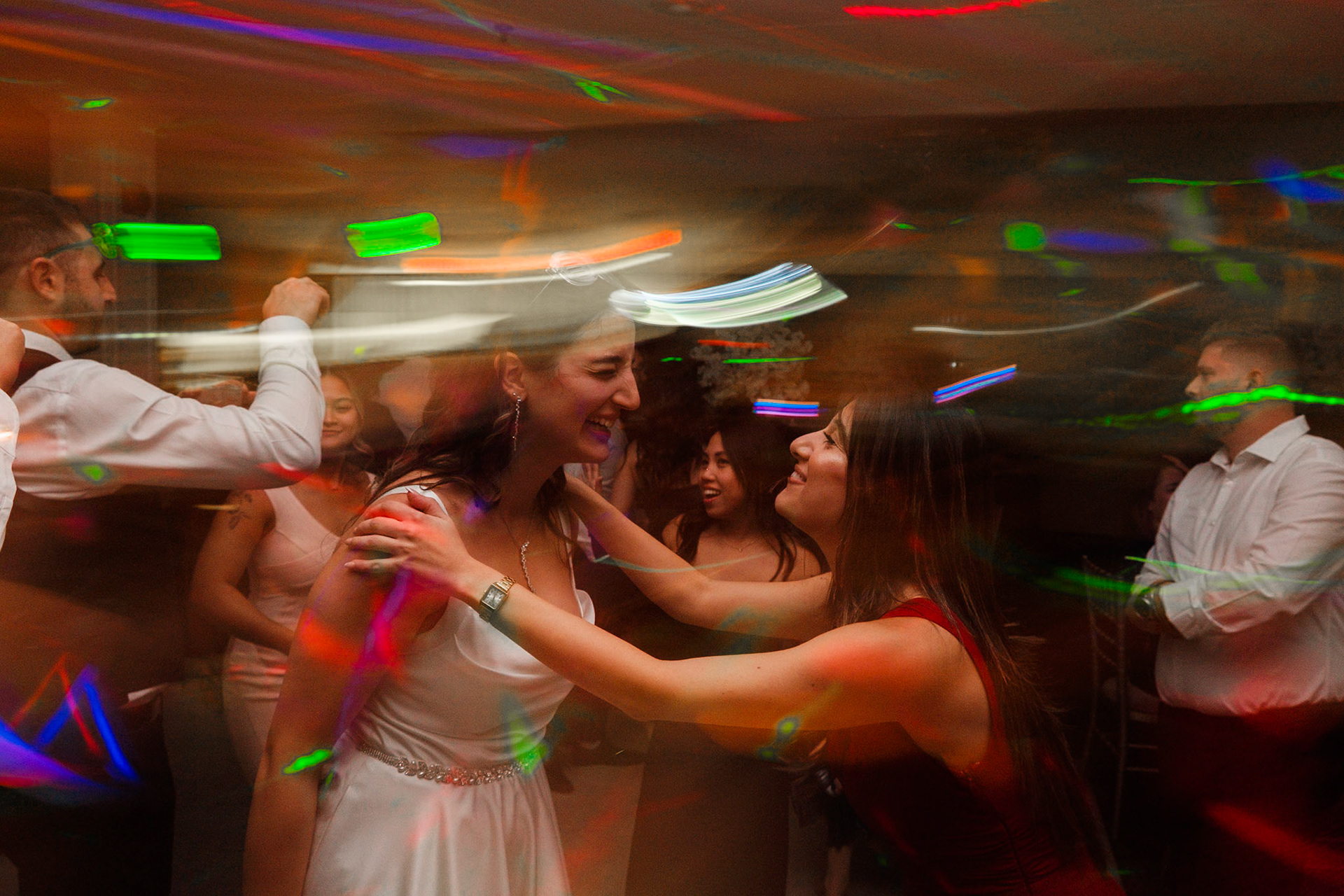 Vibrant motion-blur image of bride surrounded by guests dancing with colorful lights at Toronto party