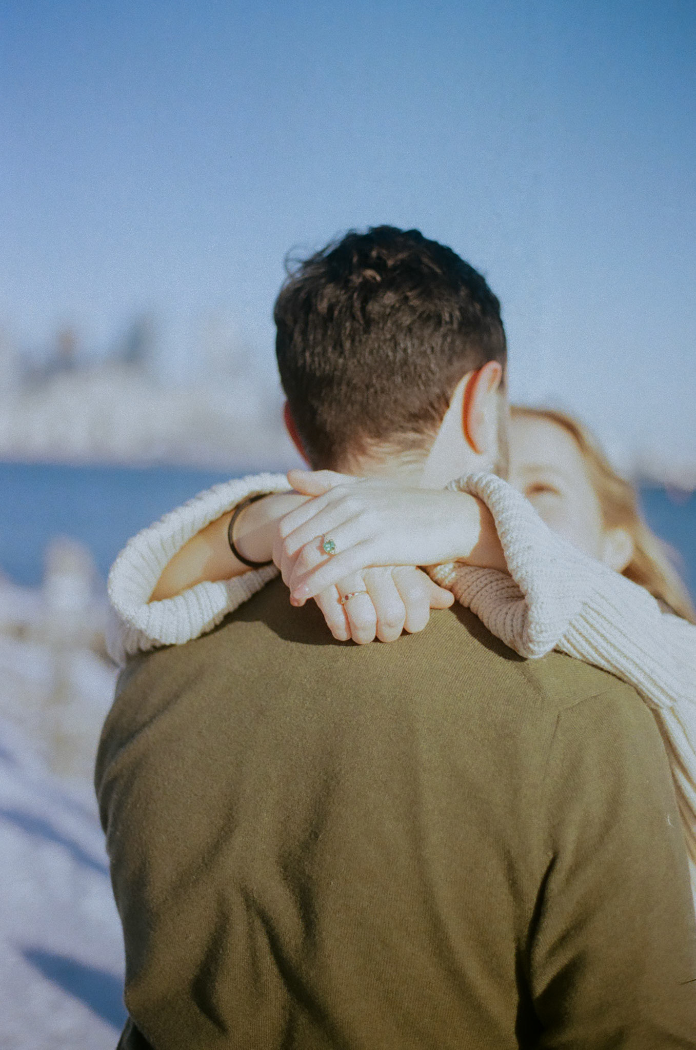 Woman wrapping arms around fiancé’s neck in tight embrace during winter engagement photoshoot