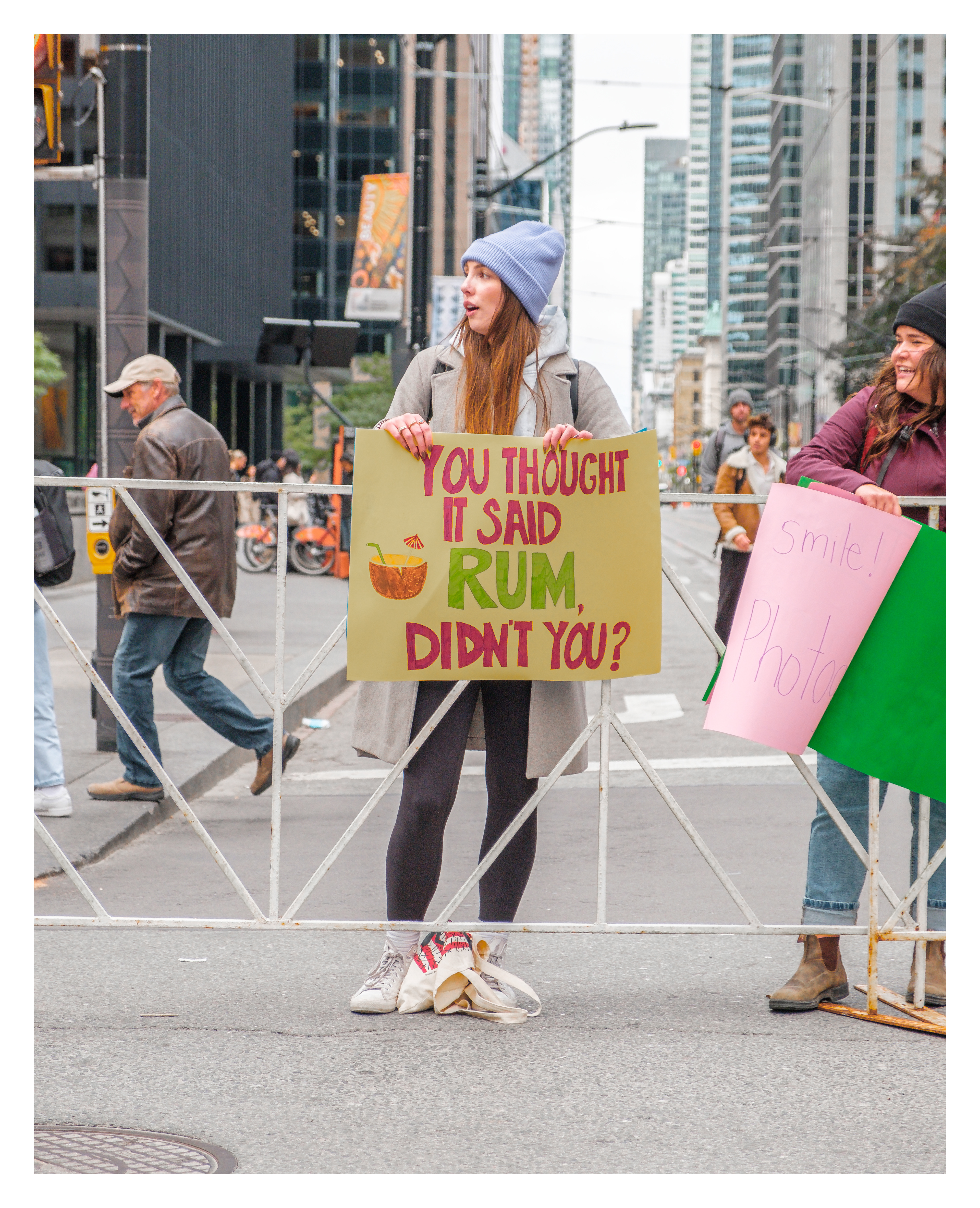 Young woman holding sign “You thought it said rum, didn’t you?” on Bay Street in Toronto, playfully encouraging marathon runners at street level.