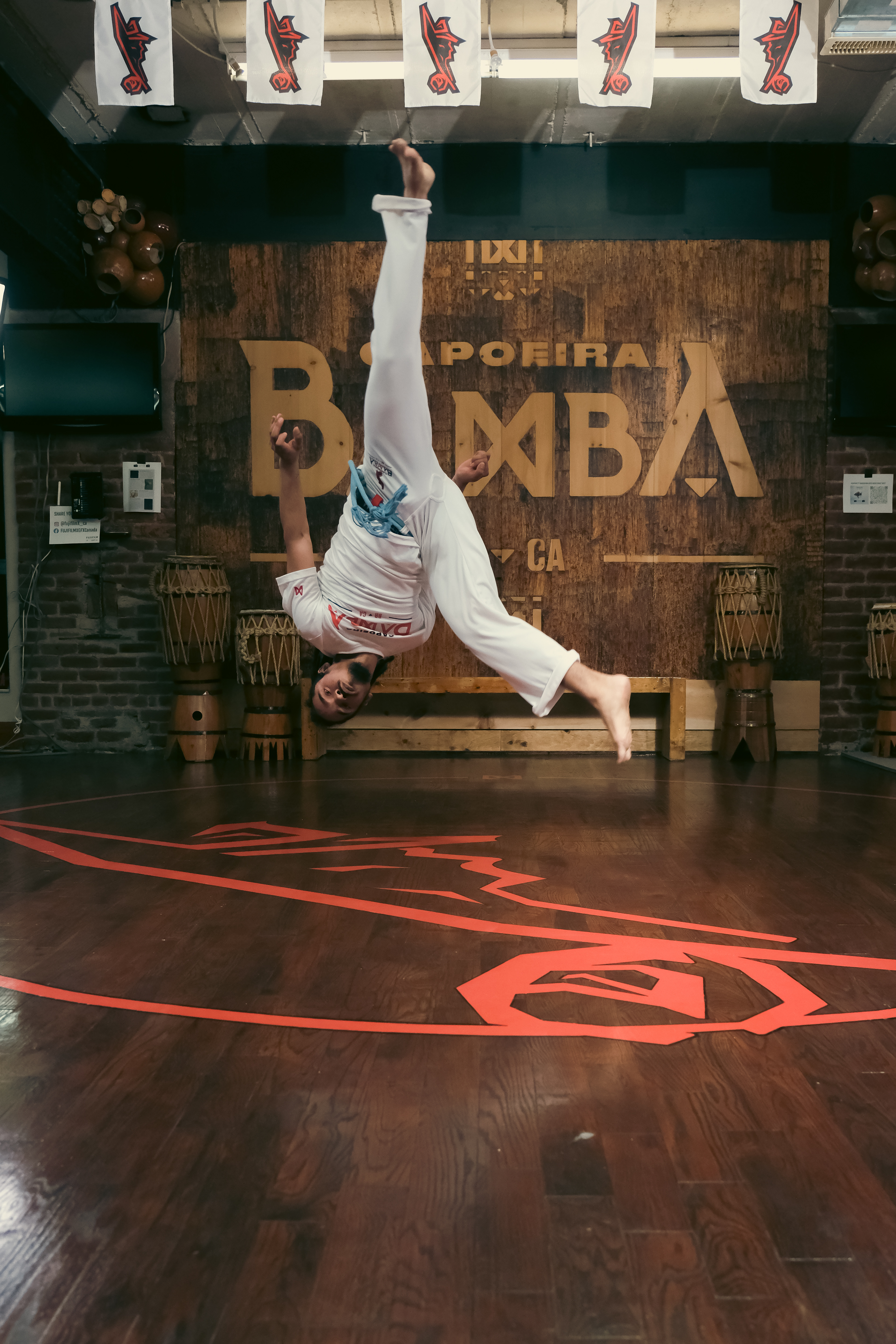 Martial artist mid-air performing a backflip kick inside the Capoeira Bamba studio.