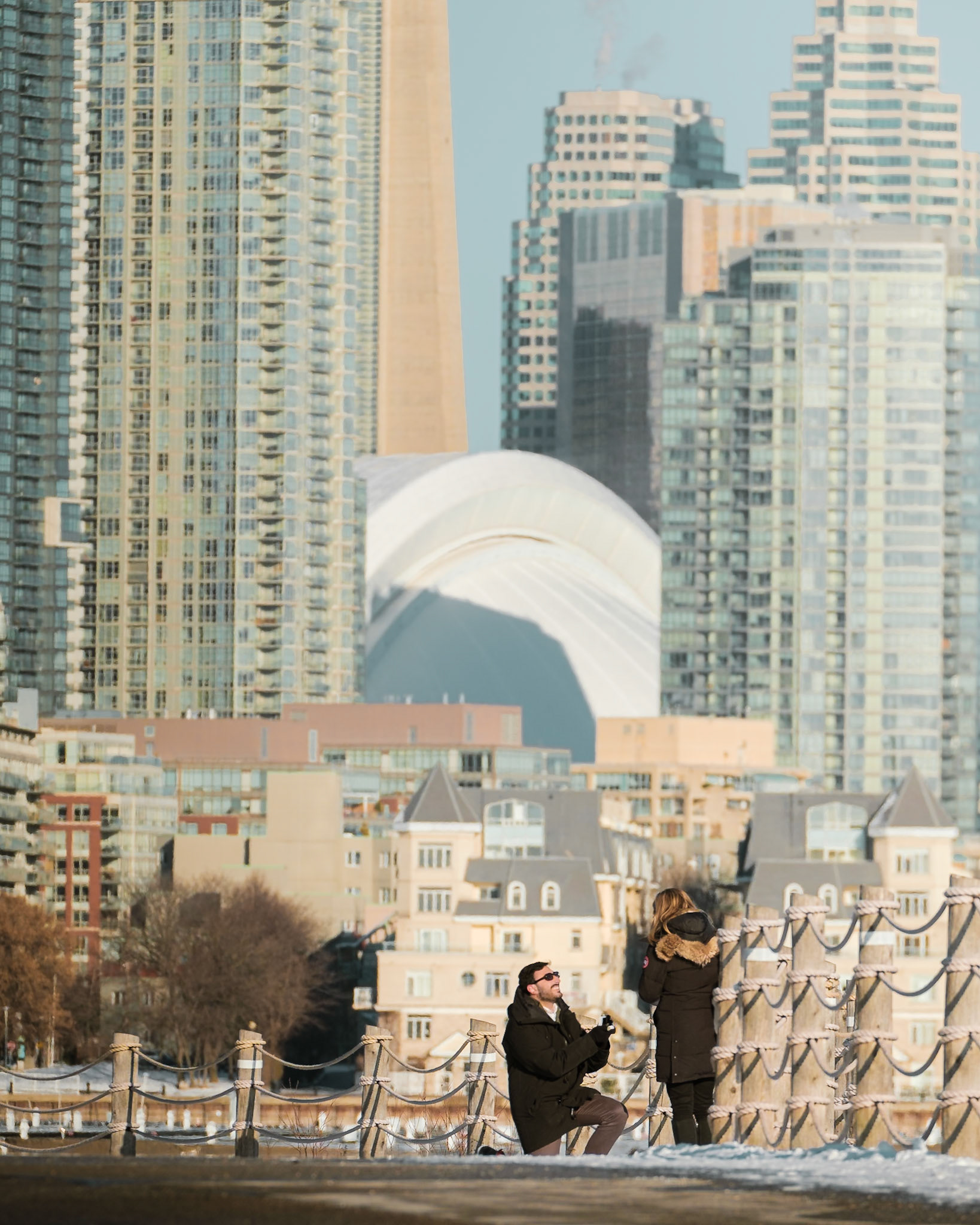 Couple embracing during proposal at Toronto’s waterfront with the Rogers Centre and CN Tower in the background