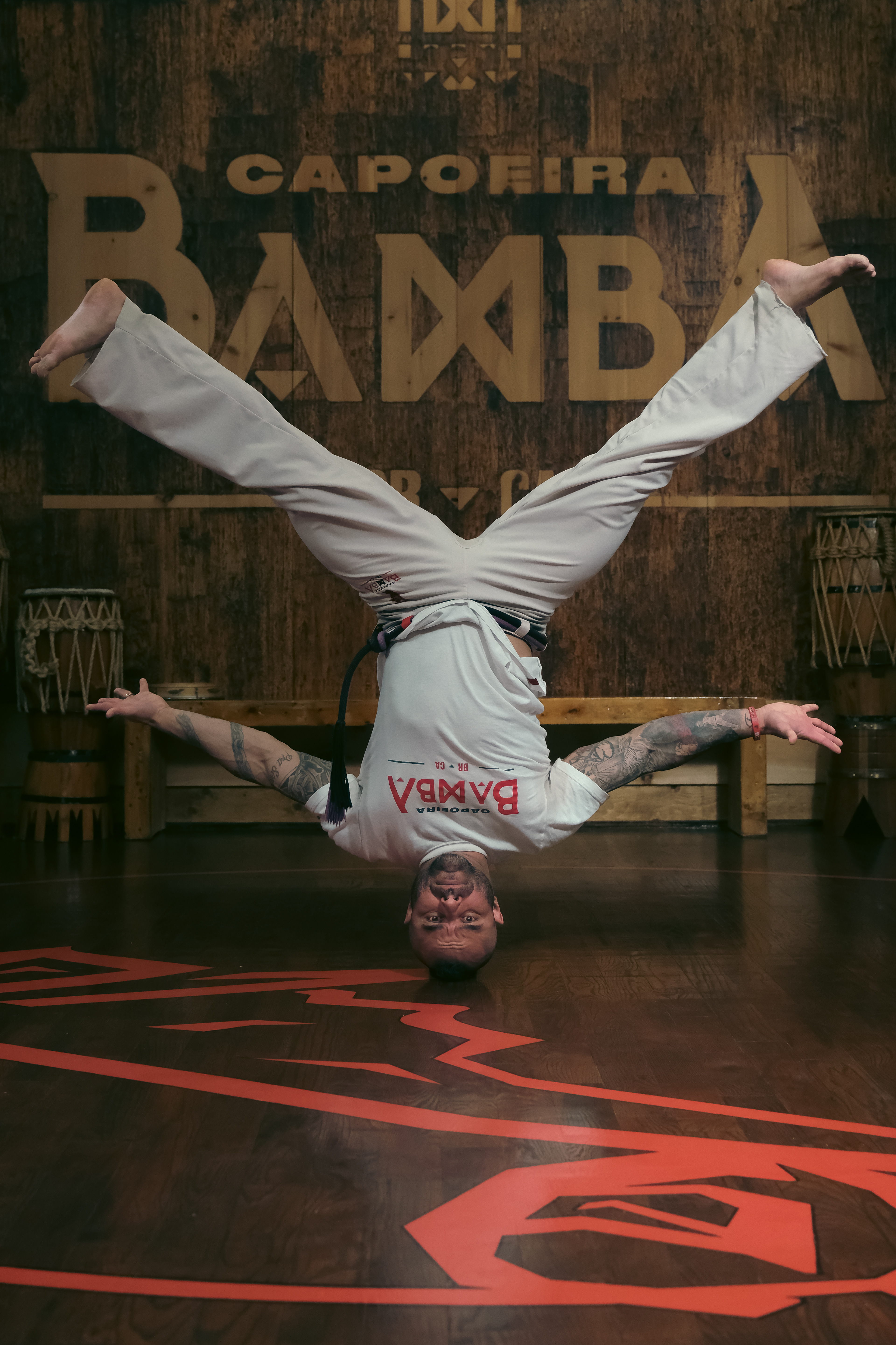 Upside-down headstand freeze pose during a Capoeira performance in front of the wooden Bamba sign.