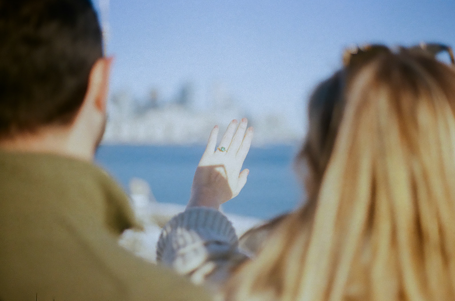 Over-the-shoulder shot of woman showing off engagement ring against Toronto’s blue skyline and lake