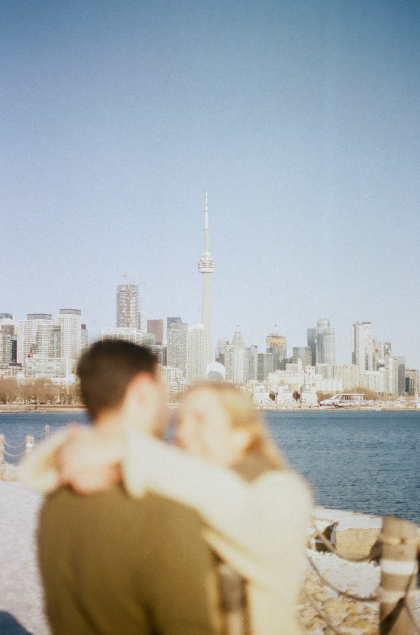 Couple standing close, arms around each other, admiring the Toronto skyline in soft winter light