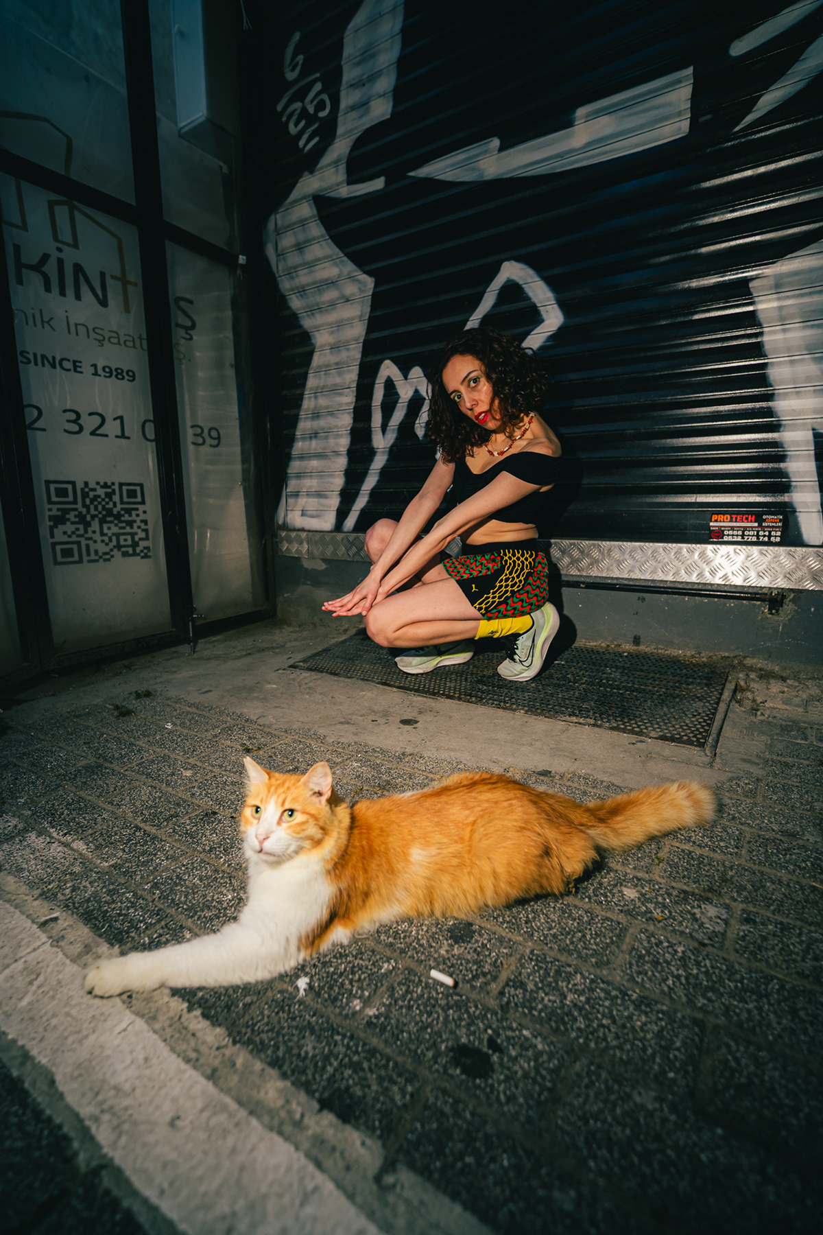 A stray cat resting beside a portrait subject on an Istanbul backstreet at night