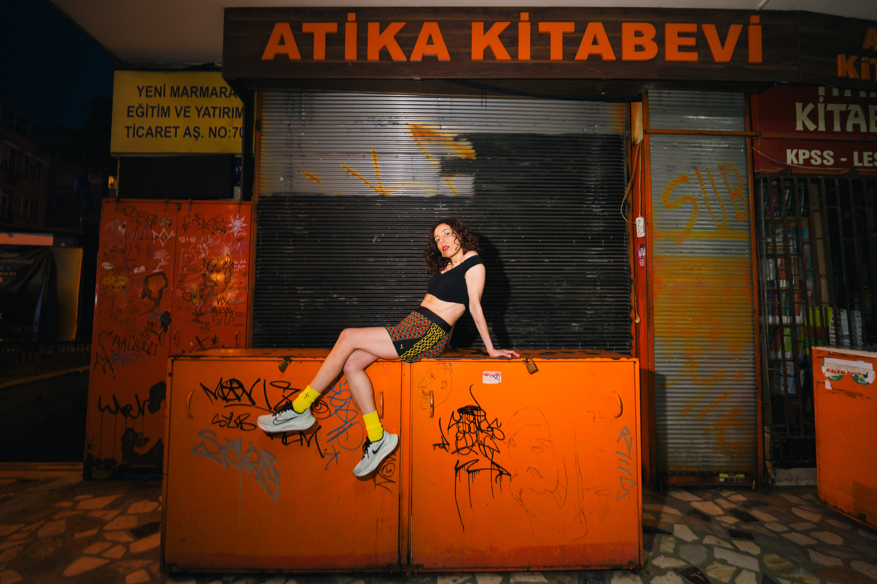 Portrait on orange steel bins outside the Atika Kitabevi bookshop at night in Istanbul