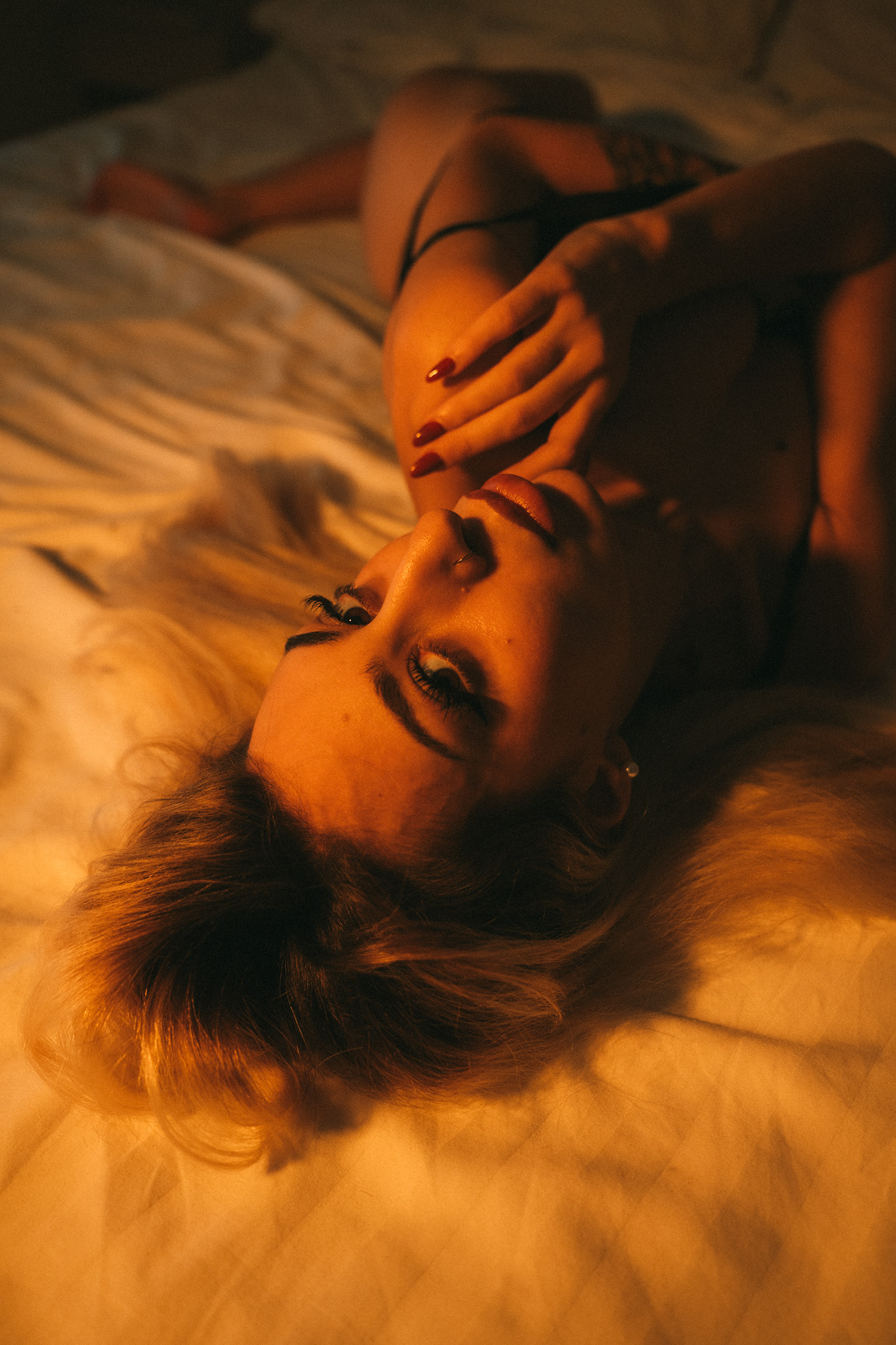 Boudoir portrait in warm amber light on a hotel bed in Bangkok