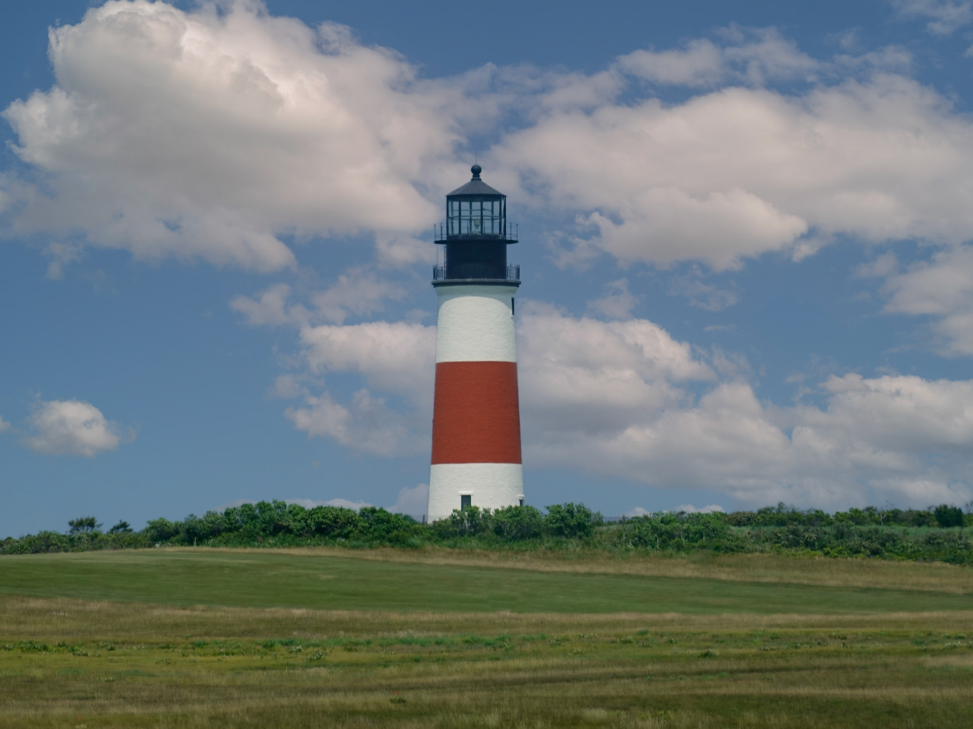 The name of this lighthouse is derived from the language of the Native Americans who lived on Nantucket, the Wampanoags. Their word “sankoty” means highland, and even erosion hasn’t changed the appropriateness of that name. The brick-and-granite structure sits 70 feet tall on the bluff at the end of what is now Baxter Road in Siasconset, flashing its white light every 7.5 seconds.  The stalwart lighthouse was built in 1850, and has not been replaced. Upon a 1990 inspection of the structure, the U.S. Army Corps of Engineers wrongly predicted that it would fall off a nearby sea cliff within 10 years. Nonetheless, in 2007 the lighthouse was very meticulously moved 400 feet back from the cliff’s edge. In 1987, it was tucked in right next to its counterpart in The National Register of Historic Places, even though it still functions as a navigational device.