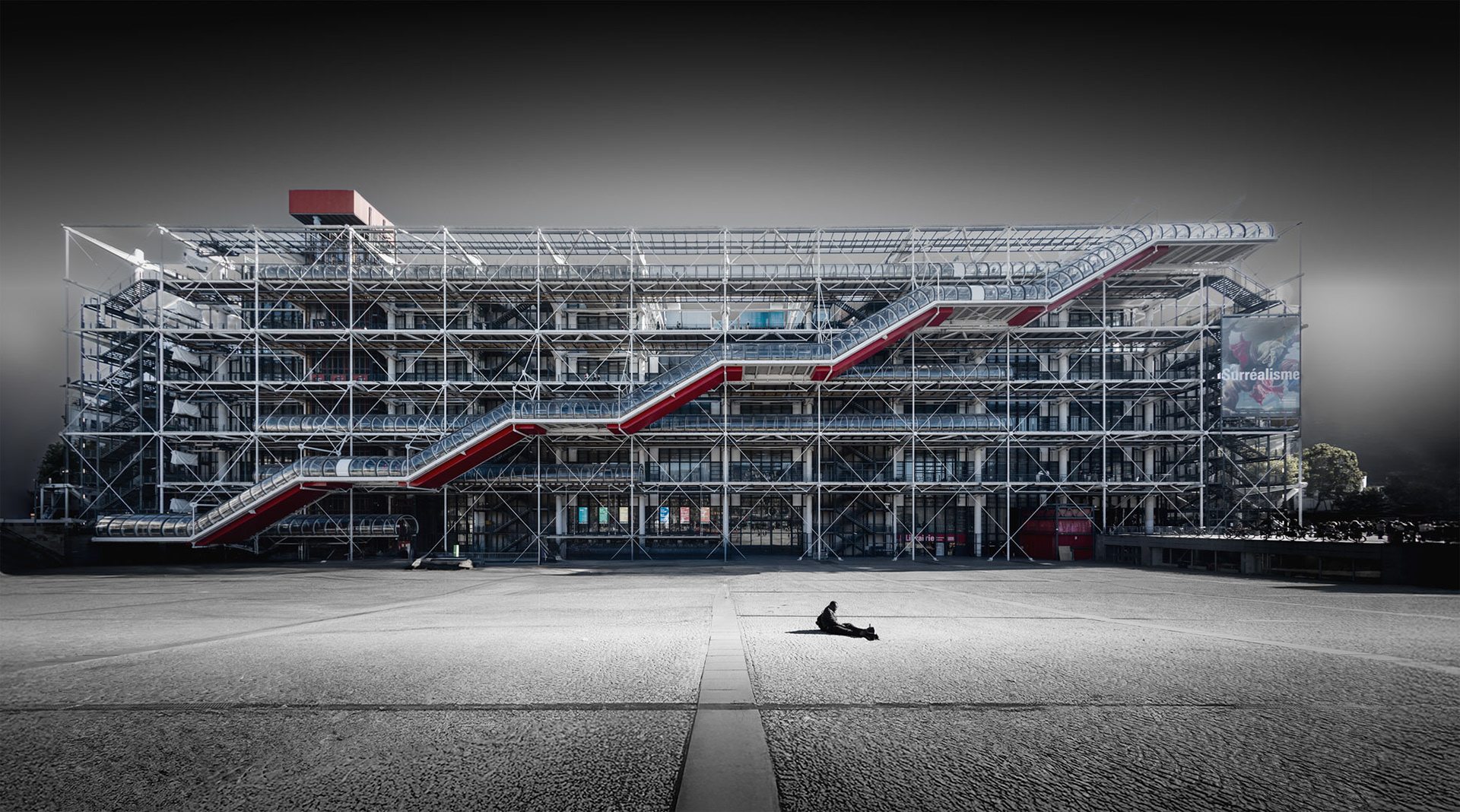 Fine art photograph of the Centre Pompidou in Paris, showing its steel and glass façade with red exterior escalators and a single figure sitting in the empty square.