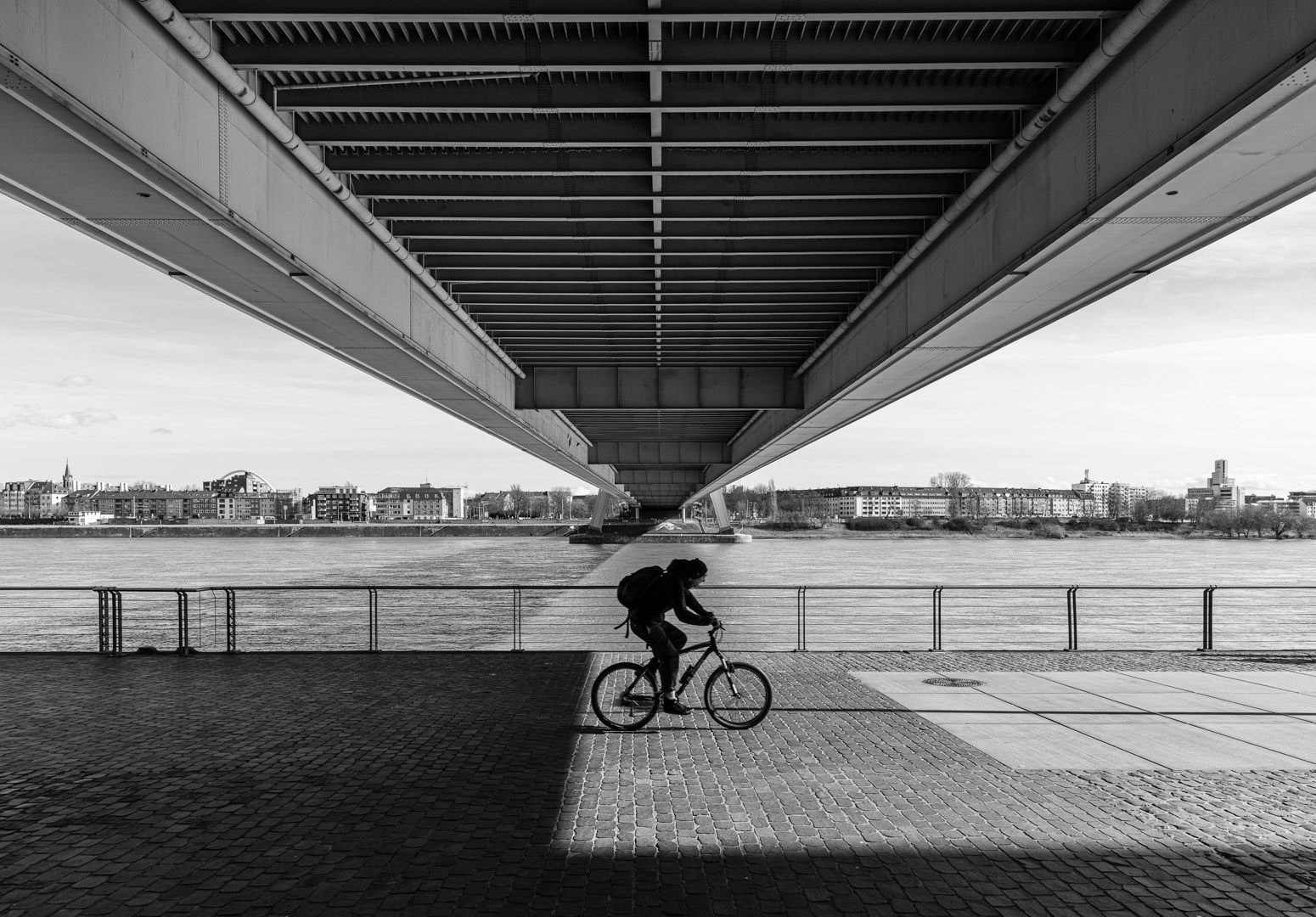 Fine art photograph of a symmetrical bridge divided by light and shadow, with a lone cyclist crossing exactly on the line between both halves.