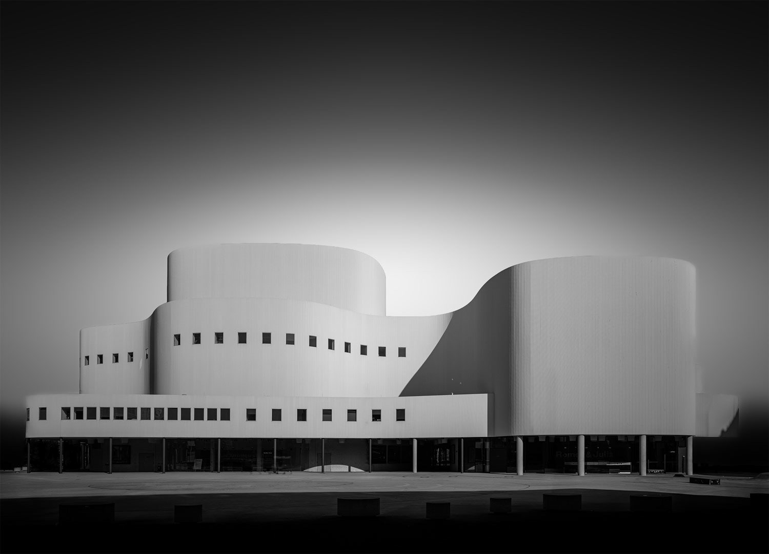 Black and white architectural photograph of a modern curved white building with strong contrasts of light and shadow in minimalist composition.