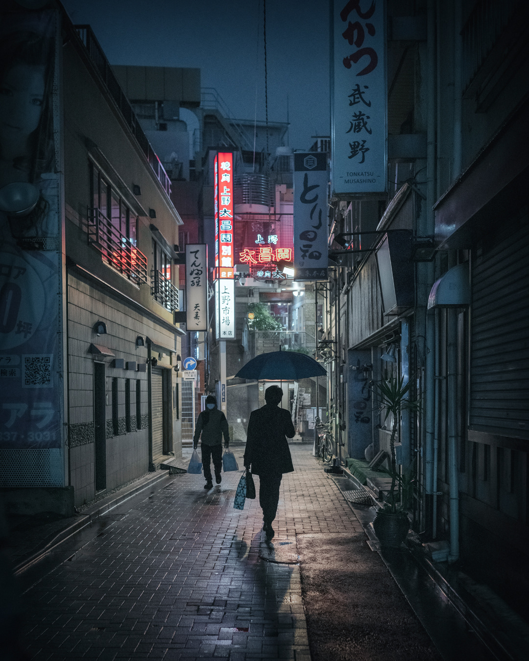 People walking through a narrow alley in the rain at night in Ueno, Tokyo.