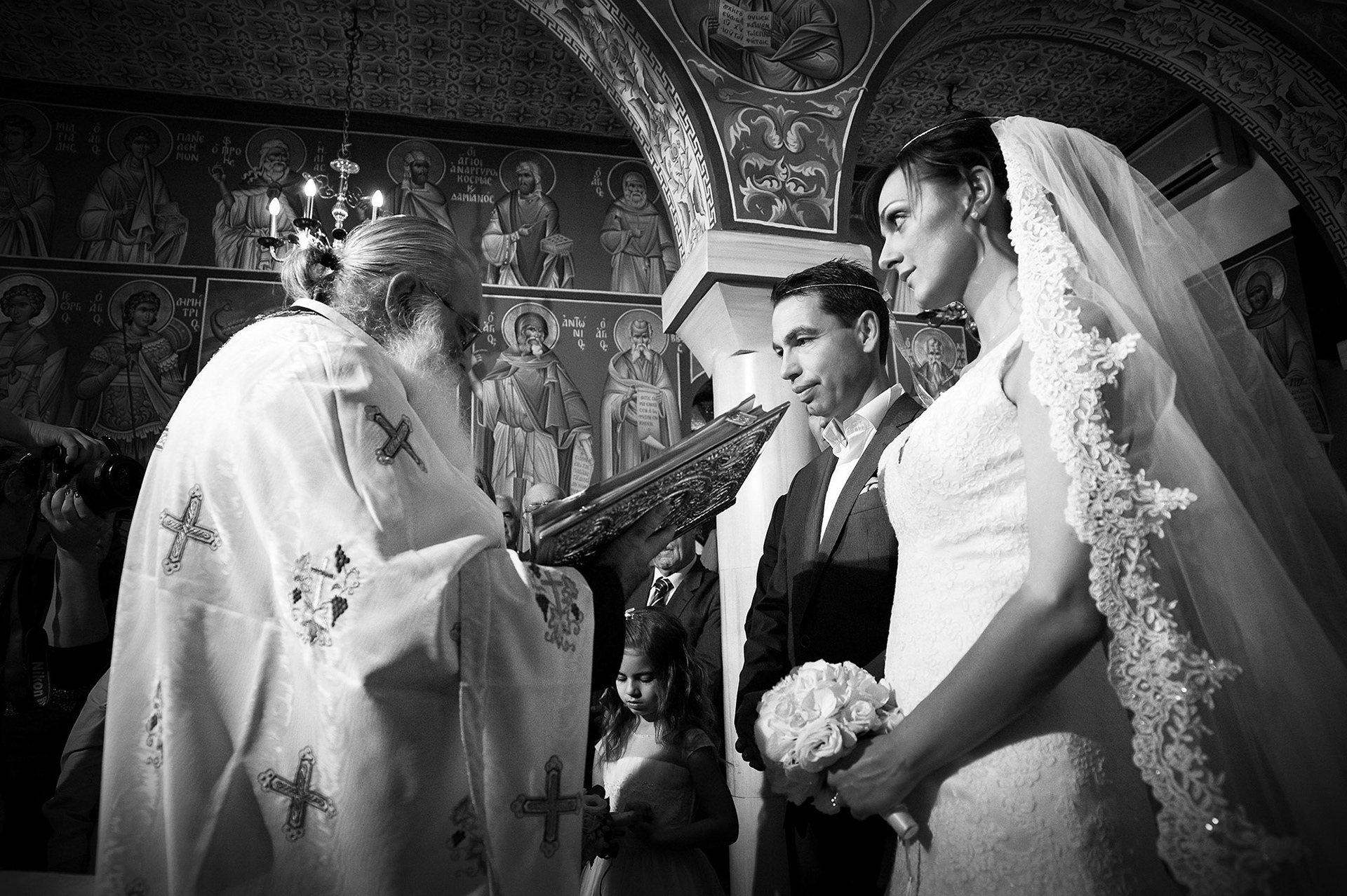 Ιερέας διαβάζει ευχές στο στεφανωμένο ζευγάρι – ασπρόμαυρη φωτογράφηση γάμου., Priest blessing the newly crowned couple – black and white wedding photography.