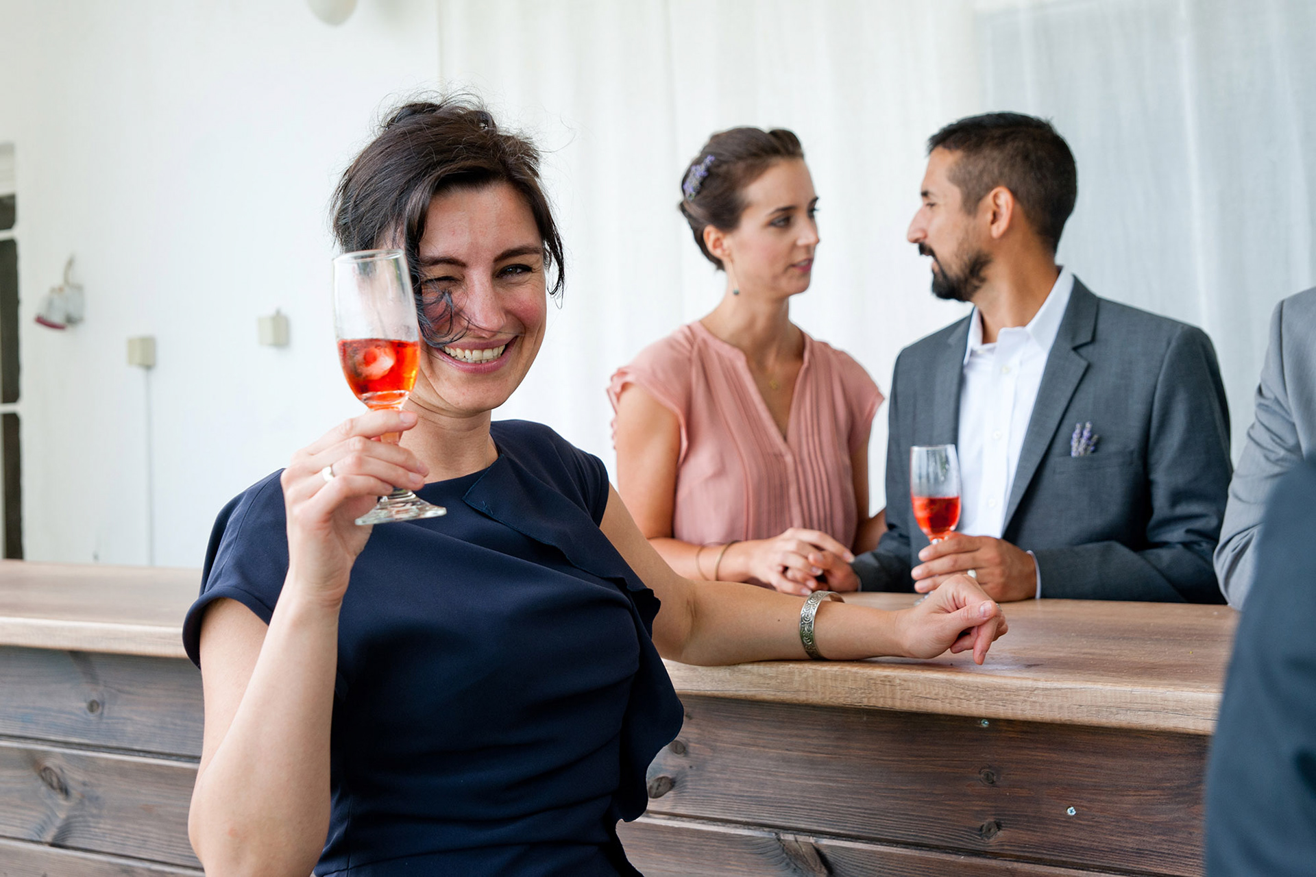 Καλεσμένη χαμογελά και σηκώνει το ποτήρι της σε πρόποση στο welcome drink του γάμου.    A guest smiling and raising her glass during the wedding welcome drink.