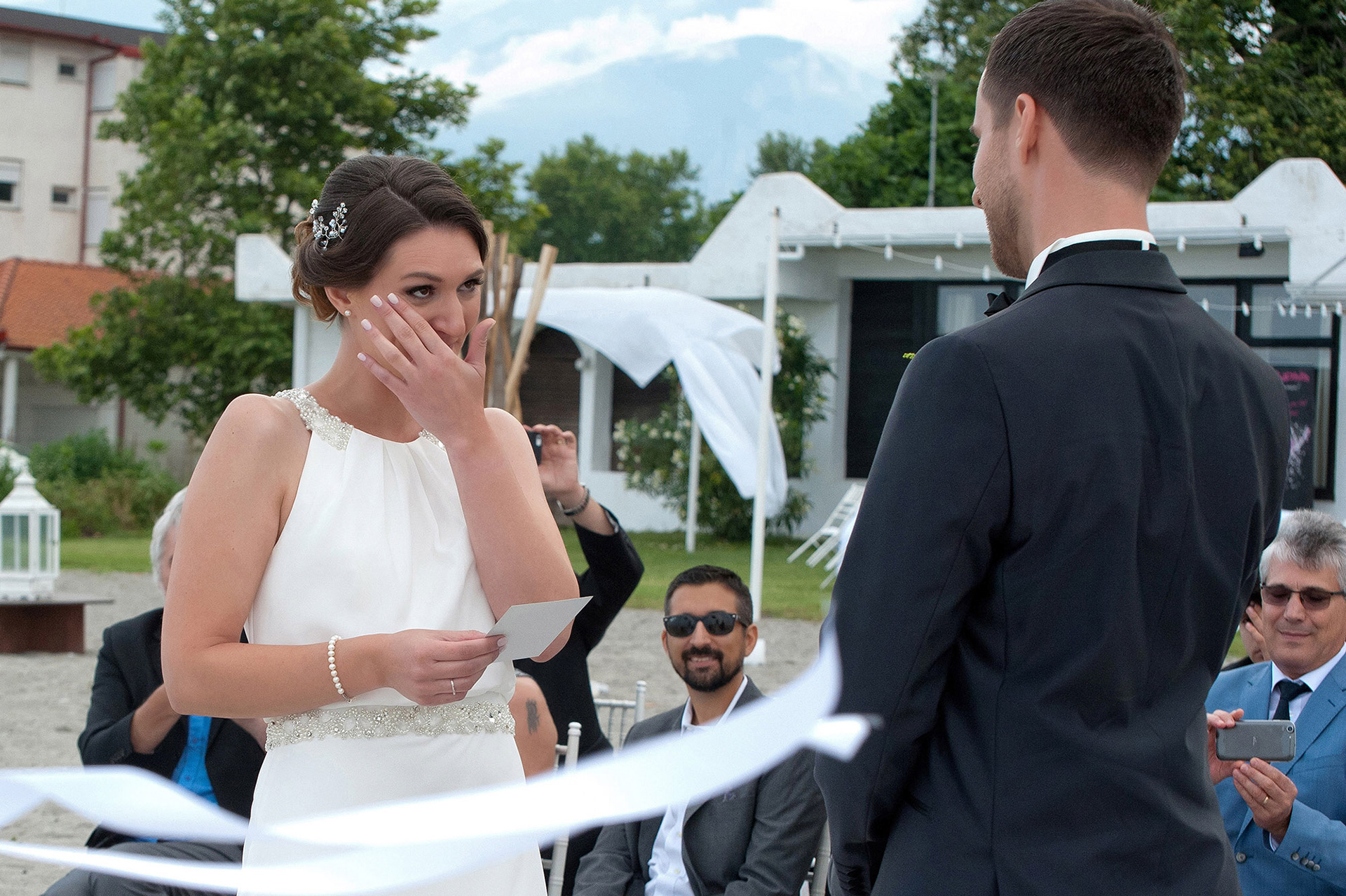 Η νύφη σκουπίζει ένα δάκρυ διαβάζοντας τους όρκους της στην παραλία του Λιτοχώρου.  The bride wiping a tear while reading her vows at the beach wedding in Litochoro.