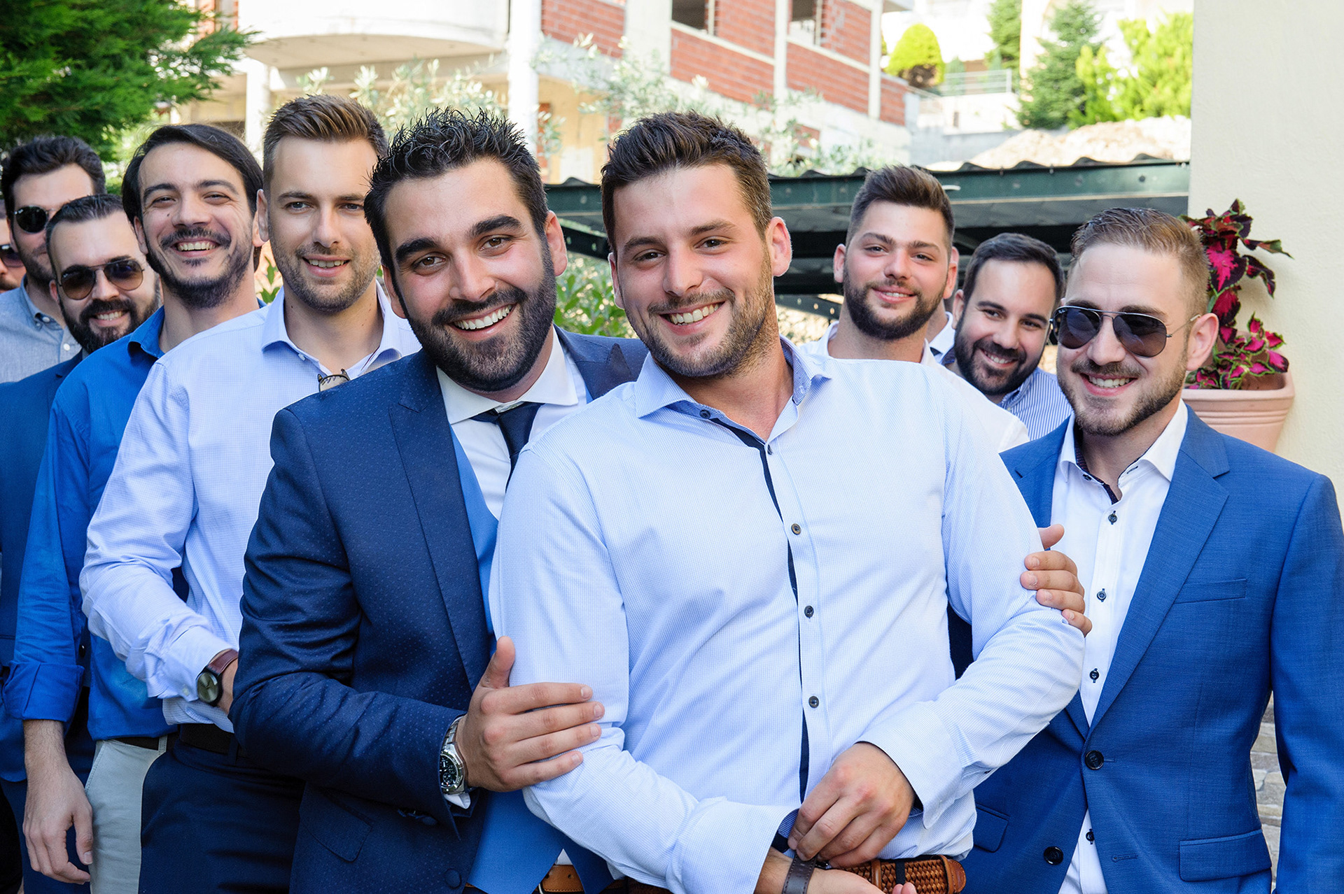 Ο γαμπρός και οι φίλοι του ποζάρουν χαμογελαστοί πριν από το μυστήριο του γάμου, γεμάτοι ενέργεια και χαρά.    The groom and his friends smiling and posing before the wedding ceremony, full of joy and excitement.