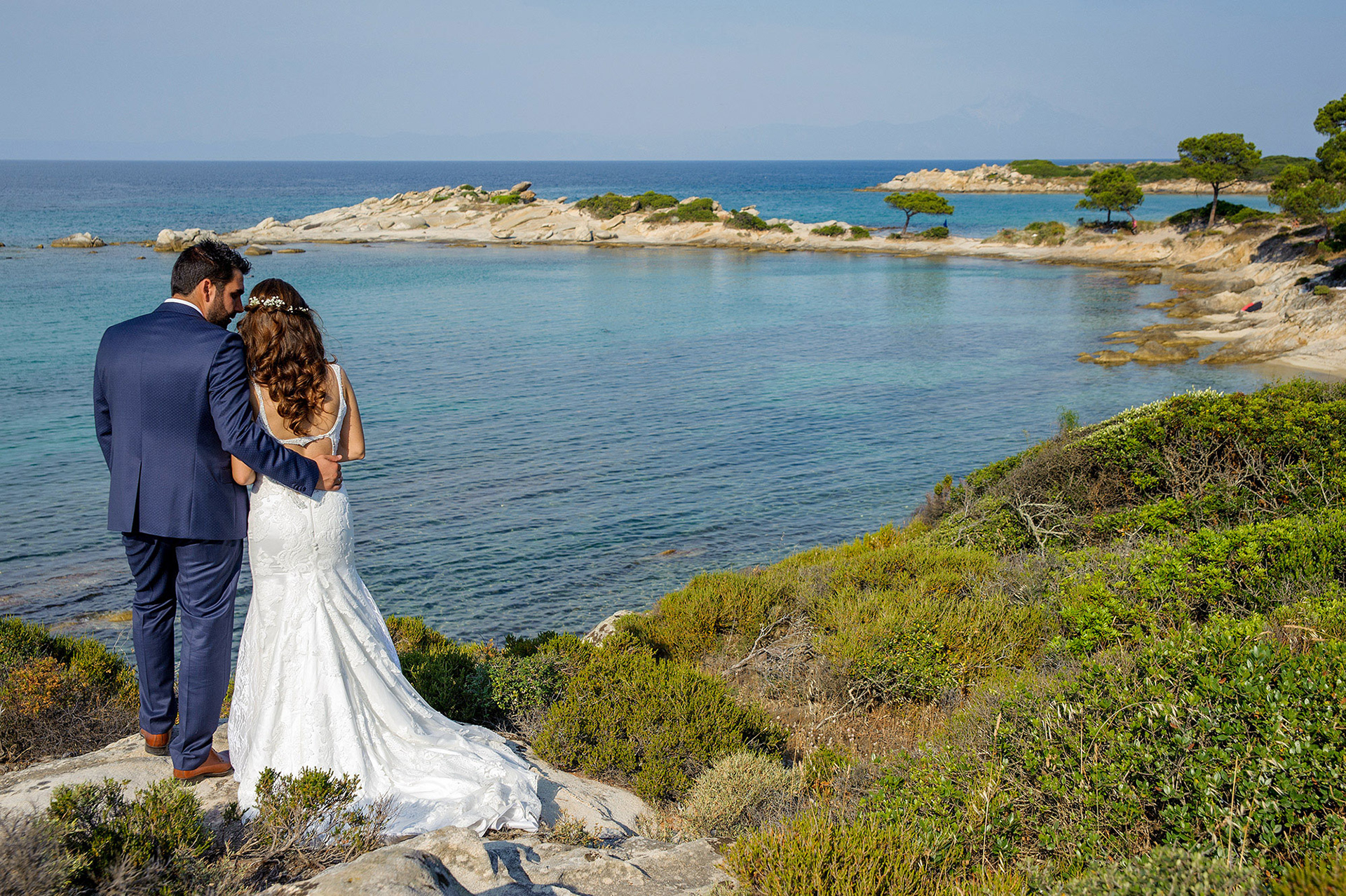 Το ζευγάρι αγκαλιασμένο κοιτάζει τη θάλασσα σε μια ήρεμη στιγμή μετά τον γάμο.  The couple stands embraced, gazing at the sea in a peaceful moment after their wedding.