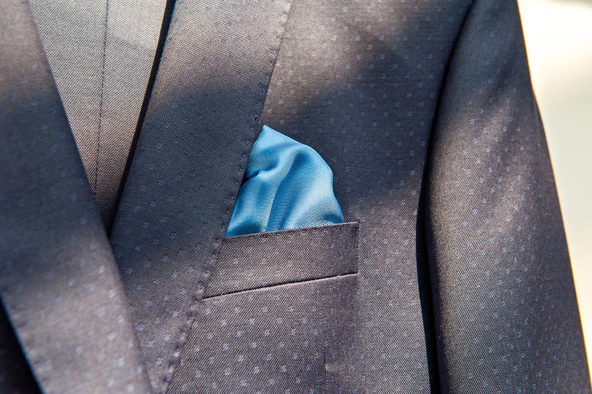 Κοντινή λεπτομέρεια από το κουστούμι του γαμπρού με μπλε μαντήλι τσέπης, φωτογράφιση γάμου στη Θεσσαλονίκη.     Close-up detail of the groom’s suit with blue pocket square, elegant wedding photography in Thessaloniki.