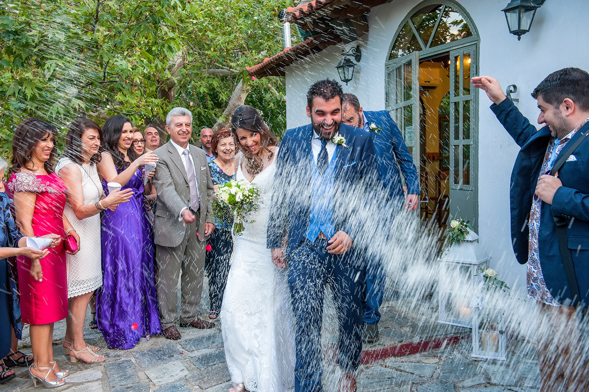 Το ζευγάρι βγαίνει από την εκκλησία ενώ οι καλεσμένοι ρίχνουν ρύζι και τους εύχονται ευτυχία.    The newlyweds exit the church as guests throw rice and wish them happiness.