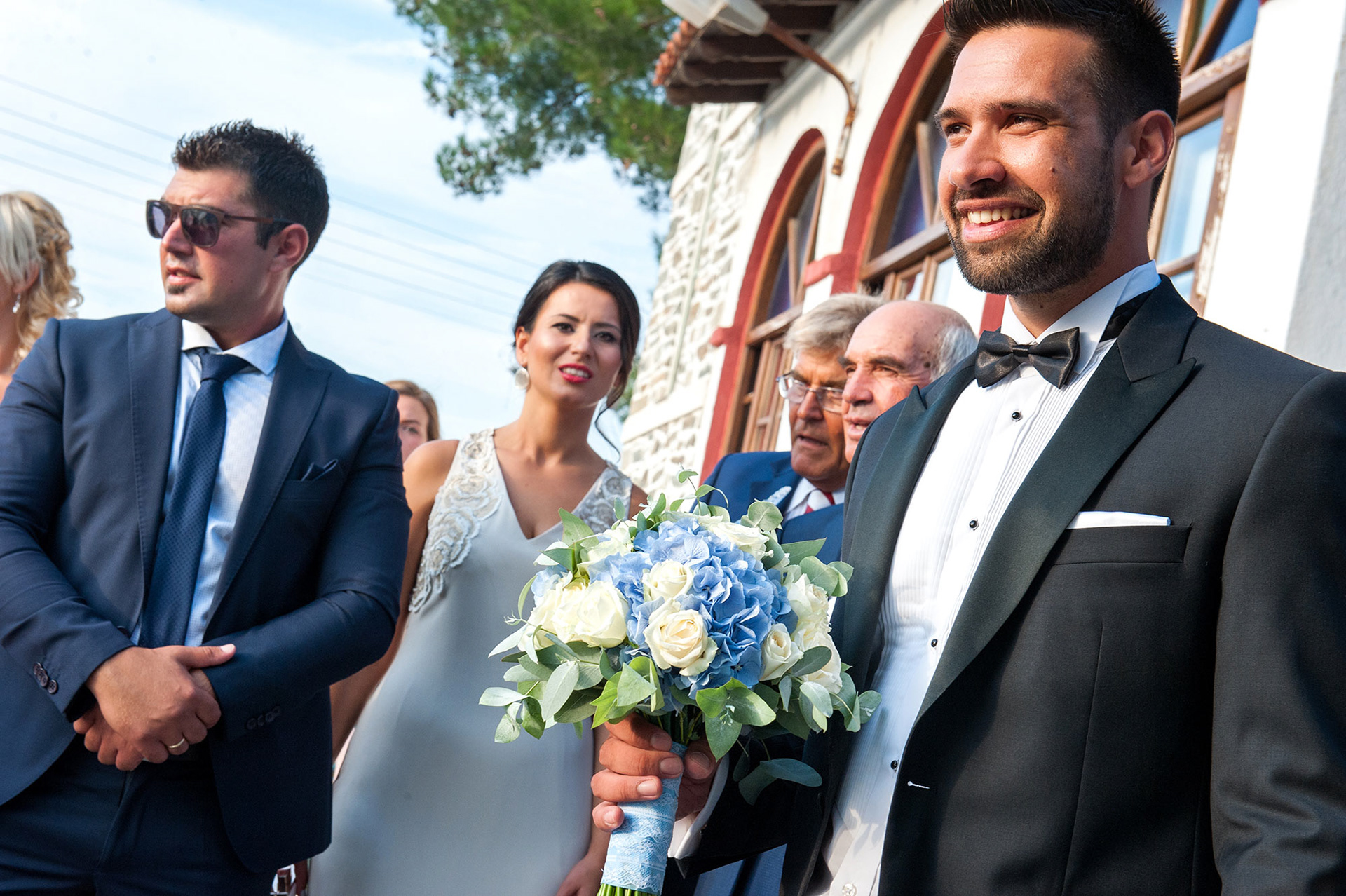 ο γαμπρός χαμογελαστός βλέπει τη νύφη να έρχεται στην εκκλησία στα πυργαδίκια χαλκιδικής , The groom smiles as he sees the bride coming to the church in Pyrgadikia, Halkidiki.