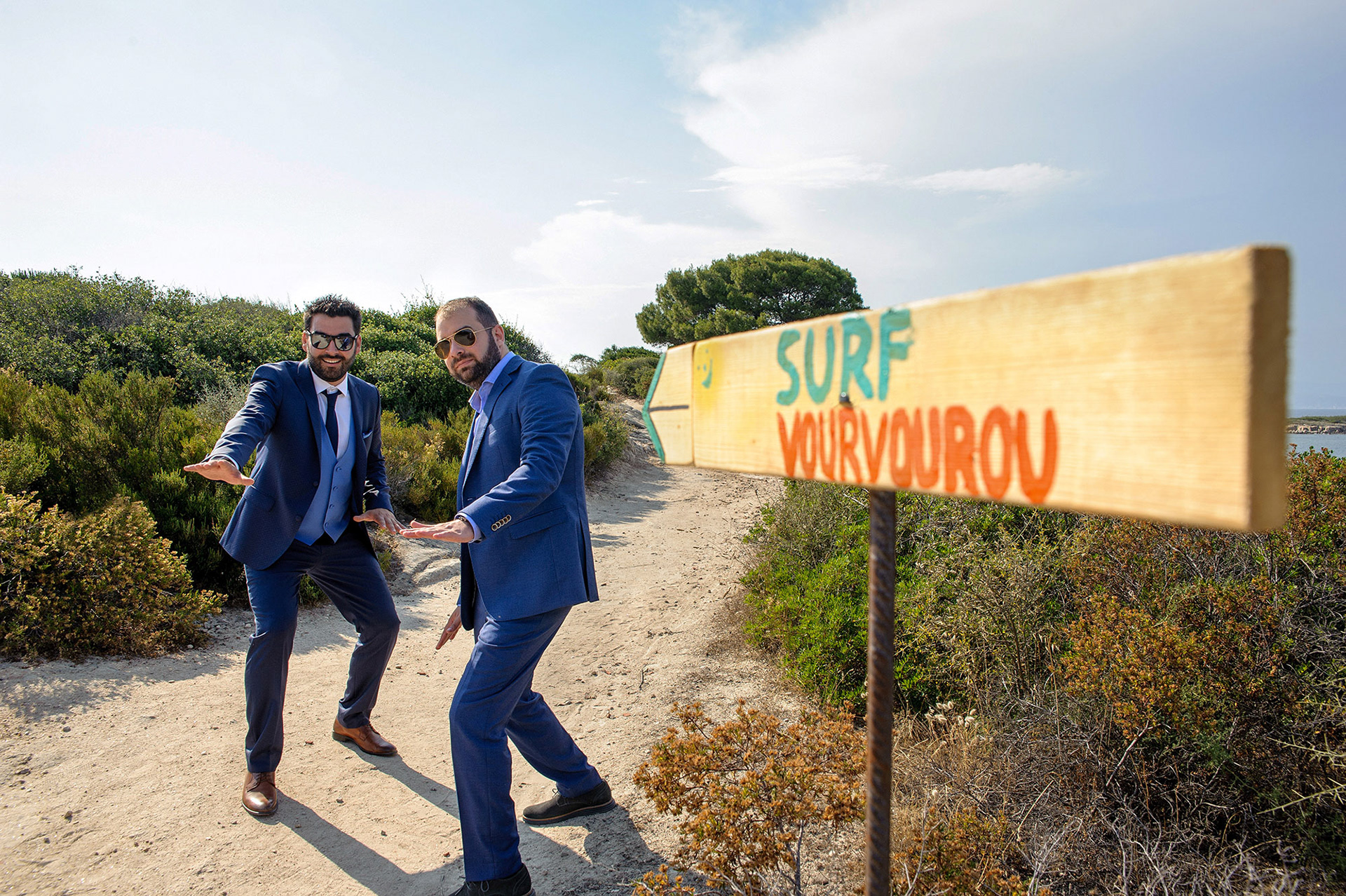 Ο γαμπρός και ο φίλος του ποζάρουν χαρούμενοι μπροστά στην ταμπέλα “Surf Vourvourou” στη Χαλκιδική.    The groom and his friend posing playfully in front of the “Surf Vourvourou” sign in Halkidiki.