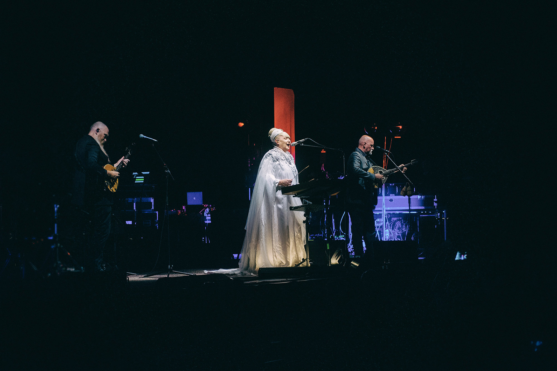 Ευρυγώνιο πλάνο με ολόκληρο το σχήμα των Dead Can Dance στη σκηνή, εστιασμένο στην αιθέρια φιγούρα της Lisa Gerrard - Wide-angle shot featuring the full Dead Can Dance lineup on stage, centered on the ethereal figure of Lisa Gerrard