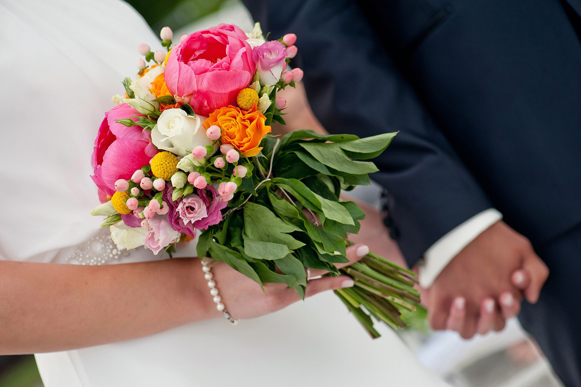 Λεπτομέρεια της ανθοδέσμης της νύφης με έντονα ροζ και πορτοκαλί λουλούδια.    Close-up of the bride’s bouquet with vibrant pink and orange flowers.