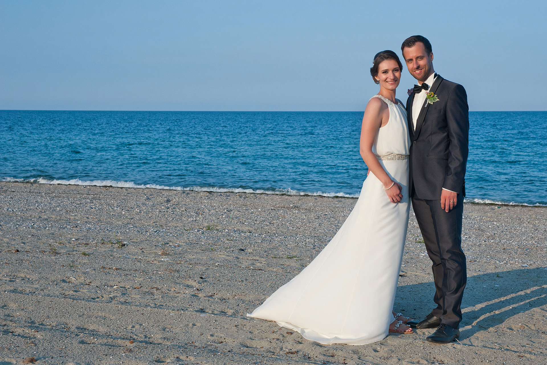 Το ζευγάρι ποζάρει χαμογελαστό στην ακροθαλασσιά με καθαρό ουρανό.  The smiling couple poses by the seashore under a clear sky.