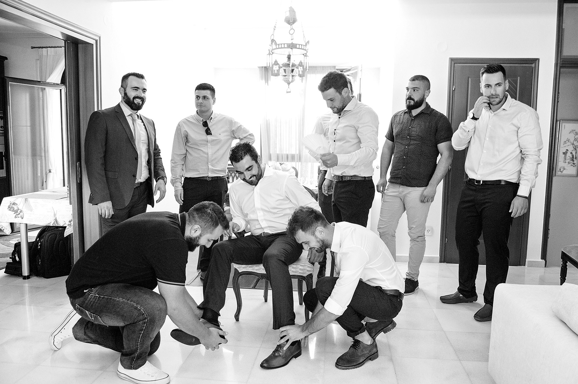 Οι φίλοι φορούν τα παπούτσια του γαμπρού, παραδοσιακό έθιμο και διασκεδαστικό στιγμιότυπο προετοιμασίας.      Friends help the groom put on his shoes, traditional and fun pre-wedding custom.