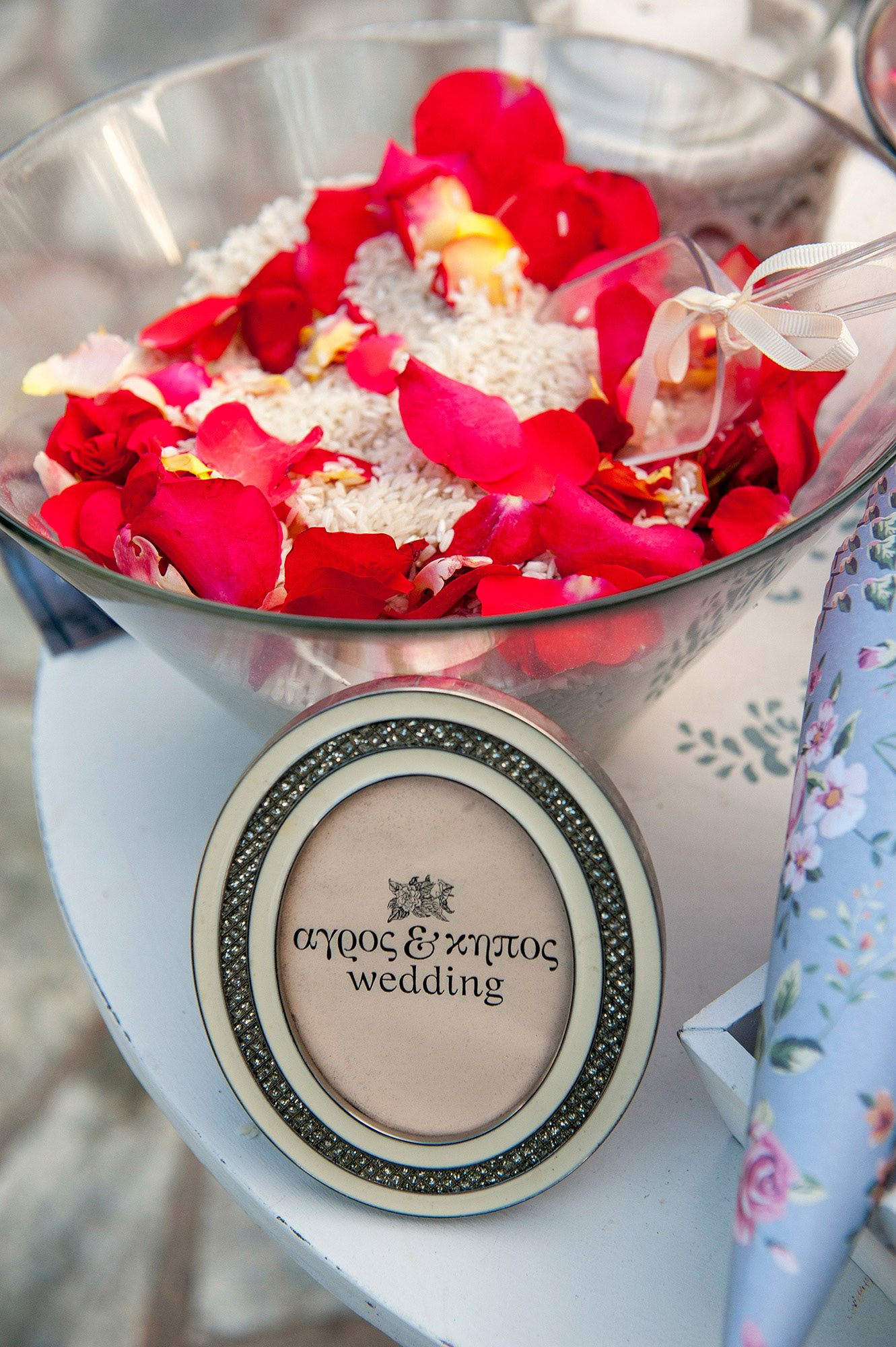 Γυάλινο μπολ με ρύζι και ροδοπέταλα για τη στιγμή του γάμου, με διακριτική πινακίδα «Άγρος & Κήπος».    Glass bowl with rice and rose petals for the wedding toss, with a small “Agros & Kipos” wedding sign.