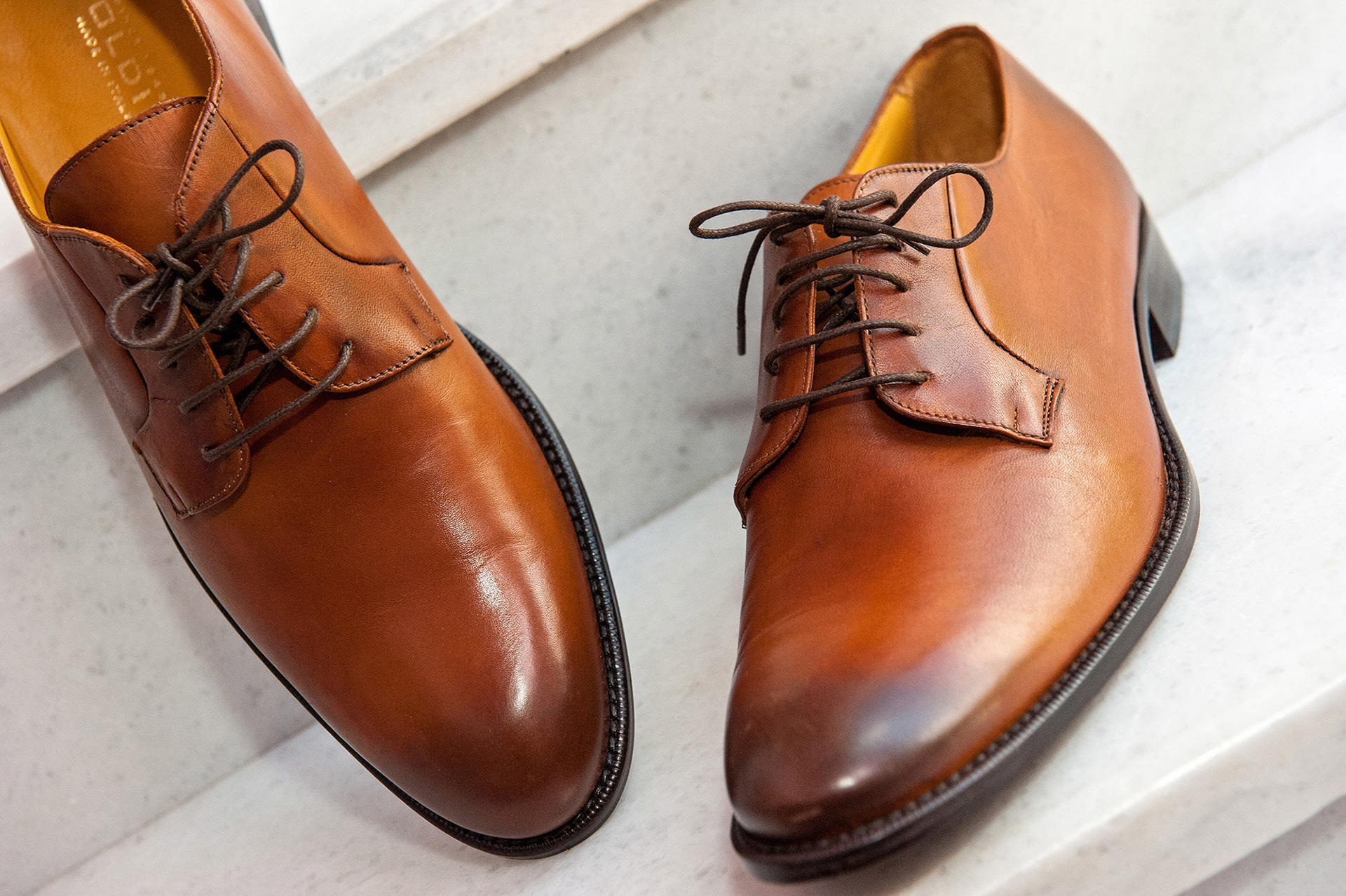 Καλλιτεχνική φωτογραφία των δερμάτινων παπουτσιών του γαμπρού, λεπτομέρεια προετοιμασίας γάμου στη Θεσσαλονίκη.     Artistic shot of the groom’s leather shoes, wedding preparation detail in Thessaloniki.