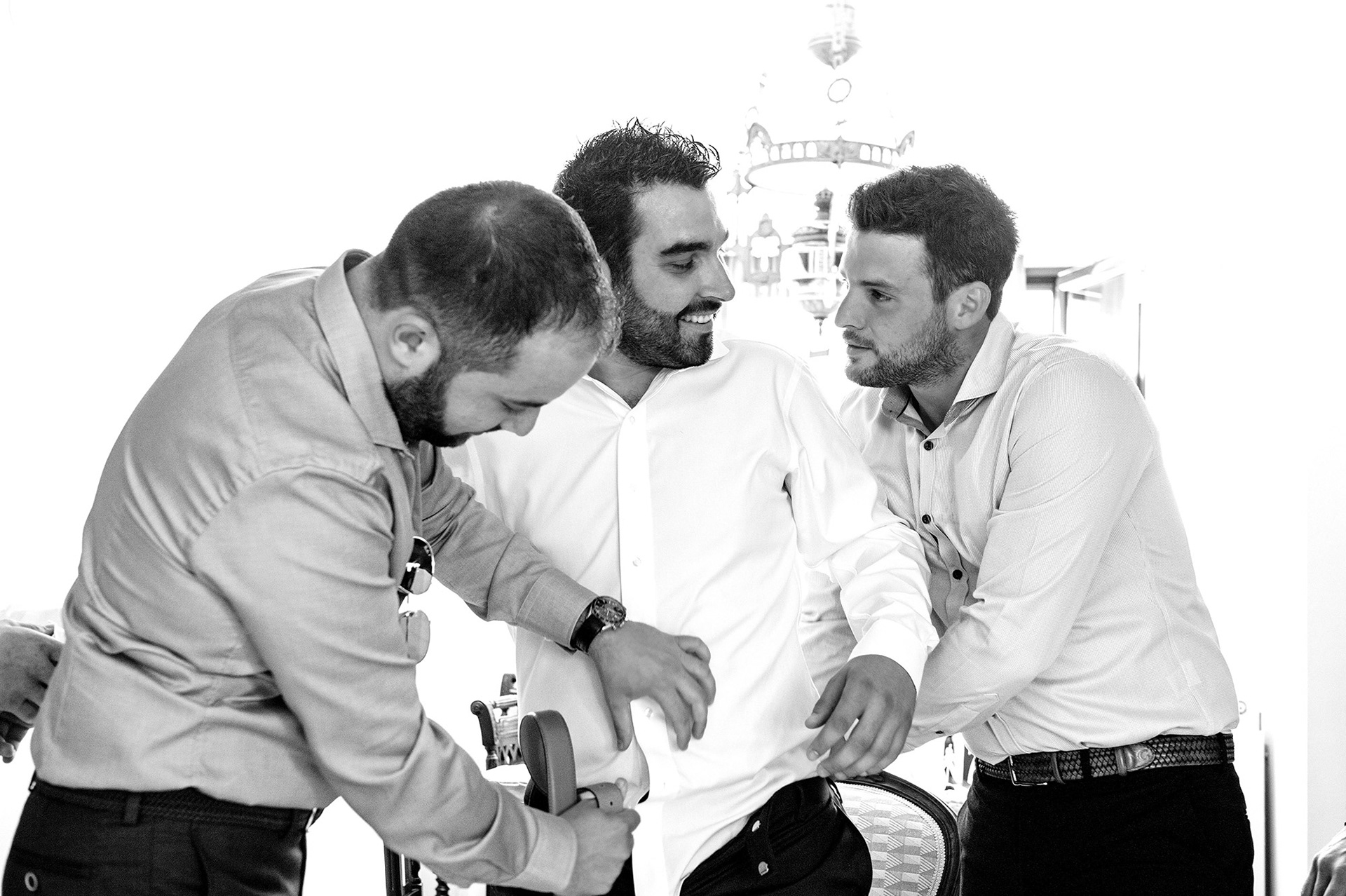 Ο γαμπρός και οι φίλοι του γελούν και μοιράζονται στιγμές πριν το μυστήριο, φυσική φωτογράφιση προετοιμασίας. The groom laughing with friends before the ceremony, candid pre-wedding photography.