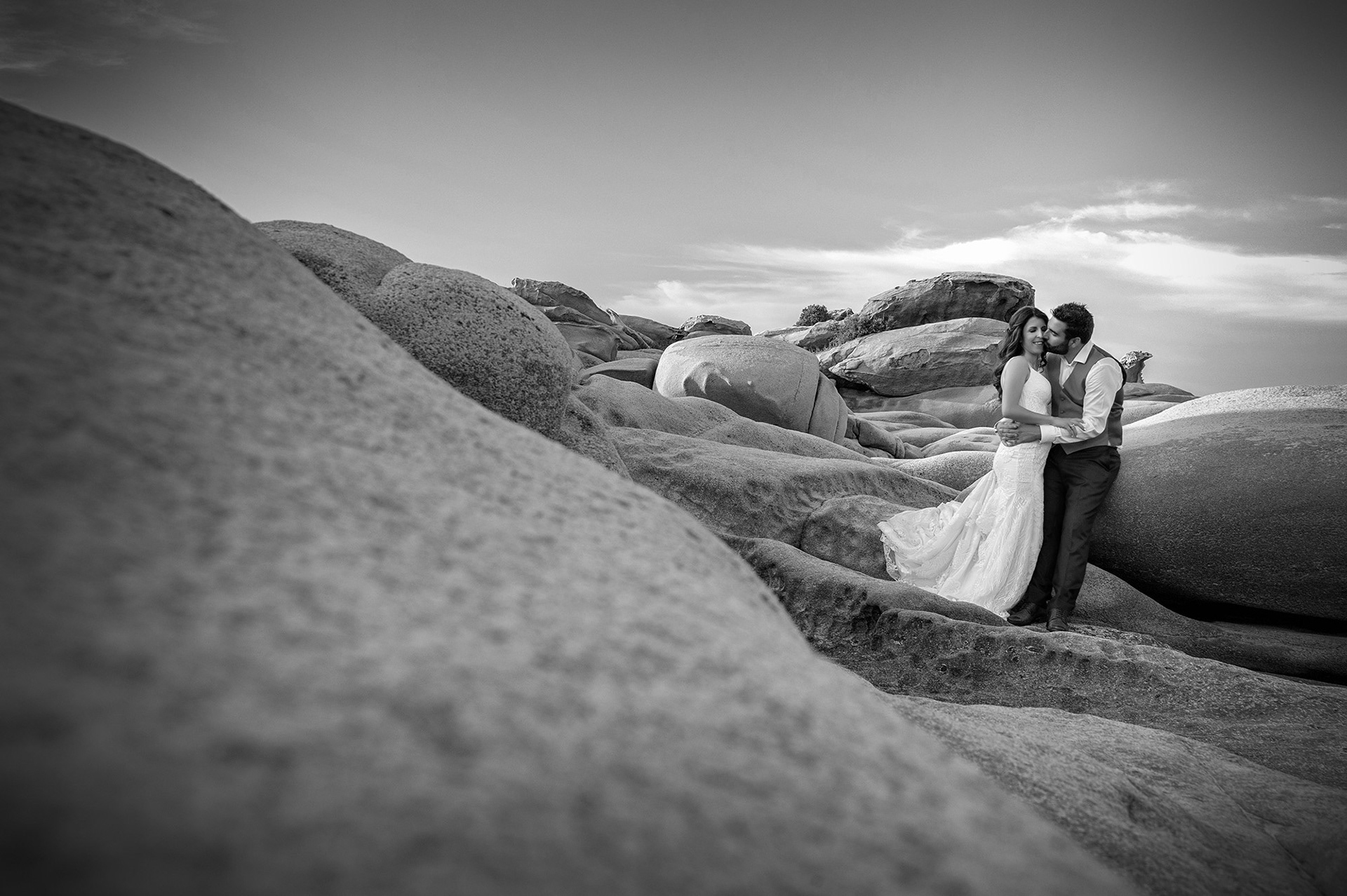 Μαυρόασπρη φωτογραφία του ζευγαριού ανάμεσα στα βράχια, με ρομαντική ατμόσφαιρα. Black and white image of the couple among the rocks in a romantic setting.