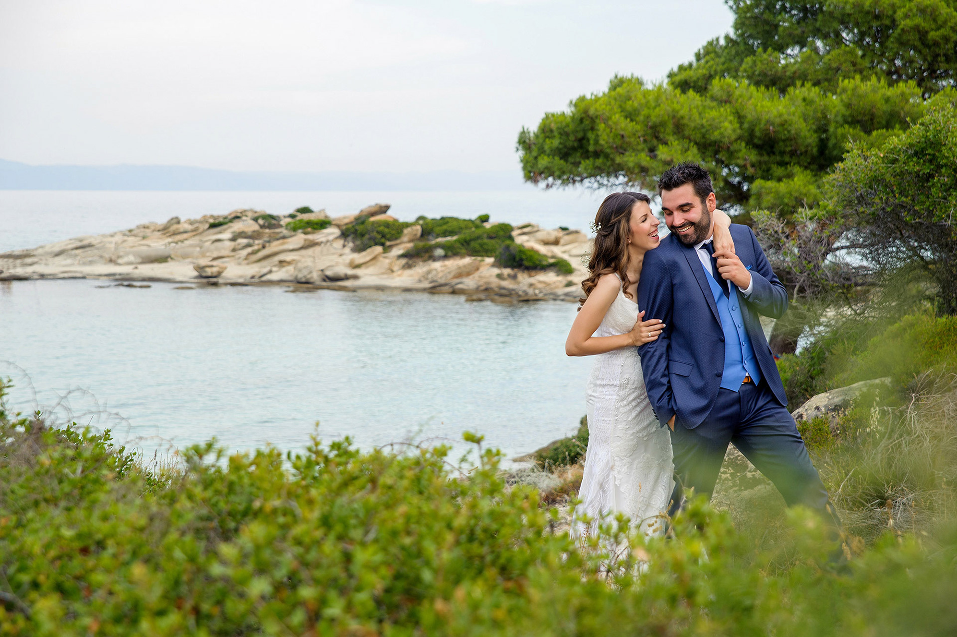 Ο γαμπρός και η νύφη  χαμογελαστοί δίπλα στη θάλασσα στη Χαλκιδική, απολαμβάνοντας τη στιγμή., φωτογράφιση γάμου,       The bride and groom  happily by the sea in Halkidiki, enjoying their post-wedding moment.   