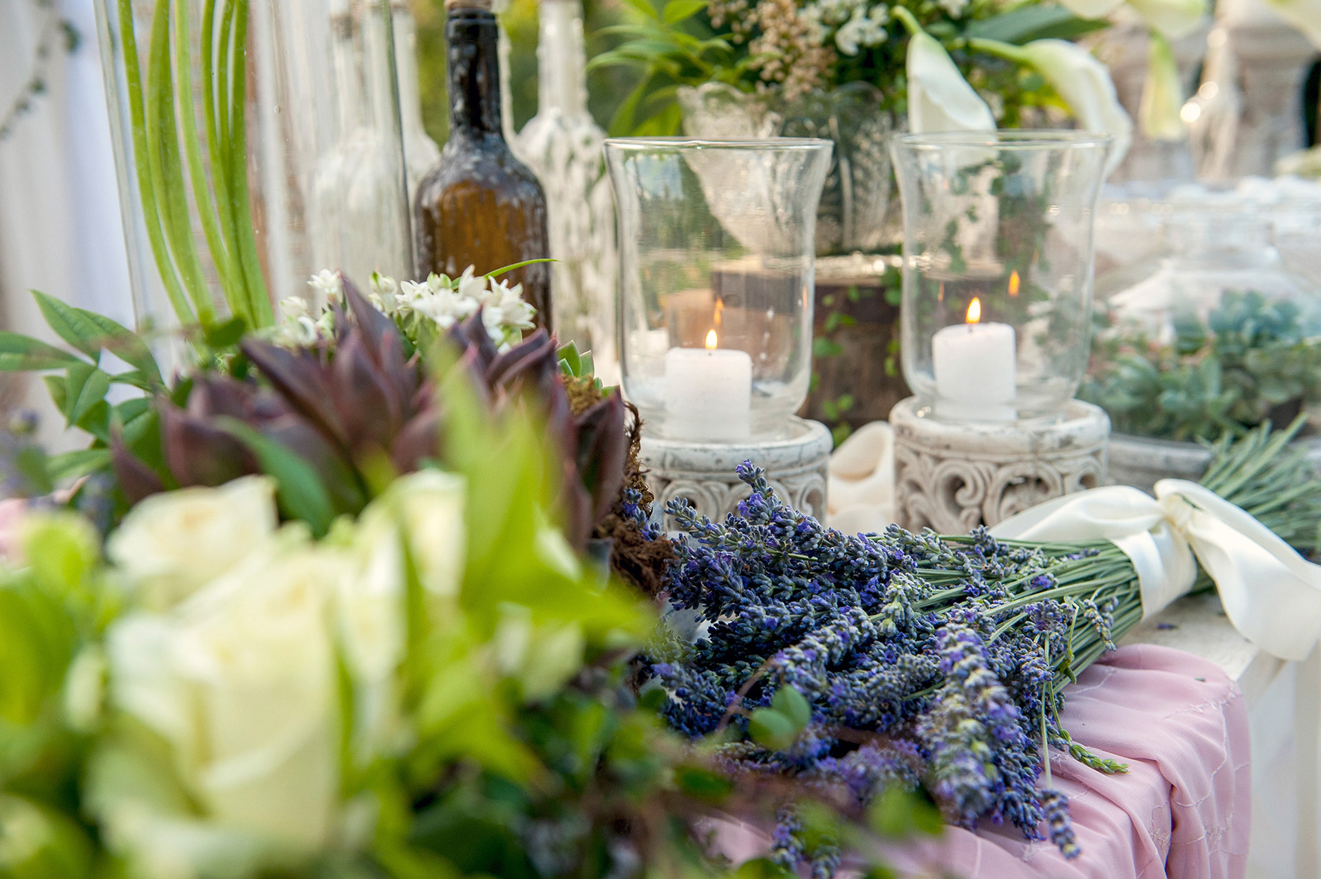 Στολισμός τραπεζιού με λεβάντα, αναμμένα κεριά και γυάλες, σε φυσικό ρομαντικό ύφος.     Table decoration with lavender, lit candles, and glass vases in a natural romantic style.