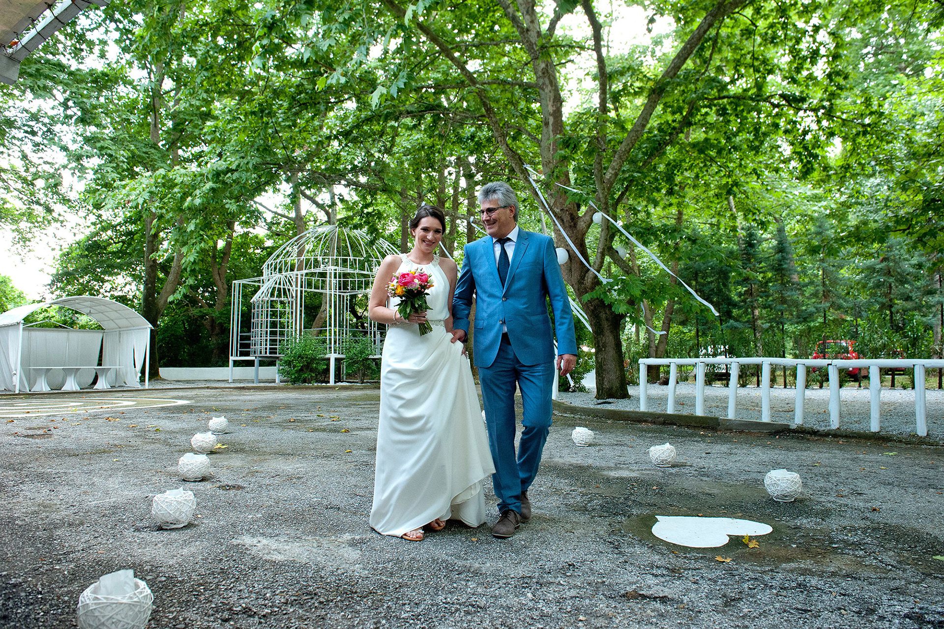 Η νύφη περπατά χαμογελαστή με τον πατέρα της προς την τελετή του γάμου στο Λιτόχωρο.    The bride walking happily with her father towards the wedding ceremony in Litochoro.