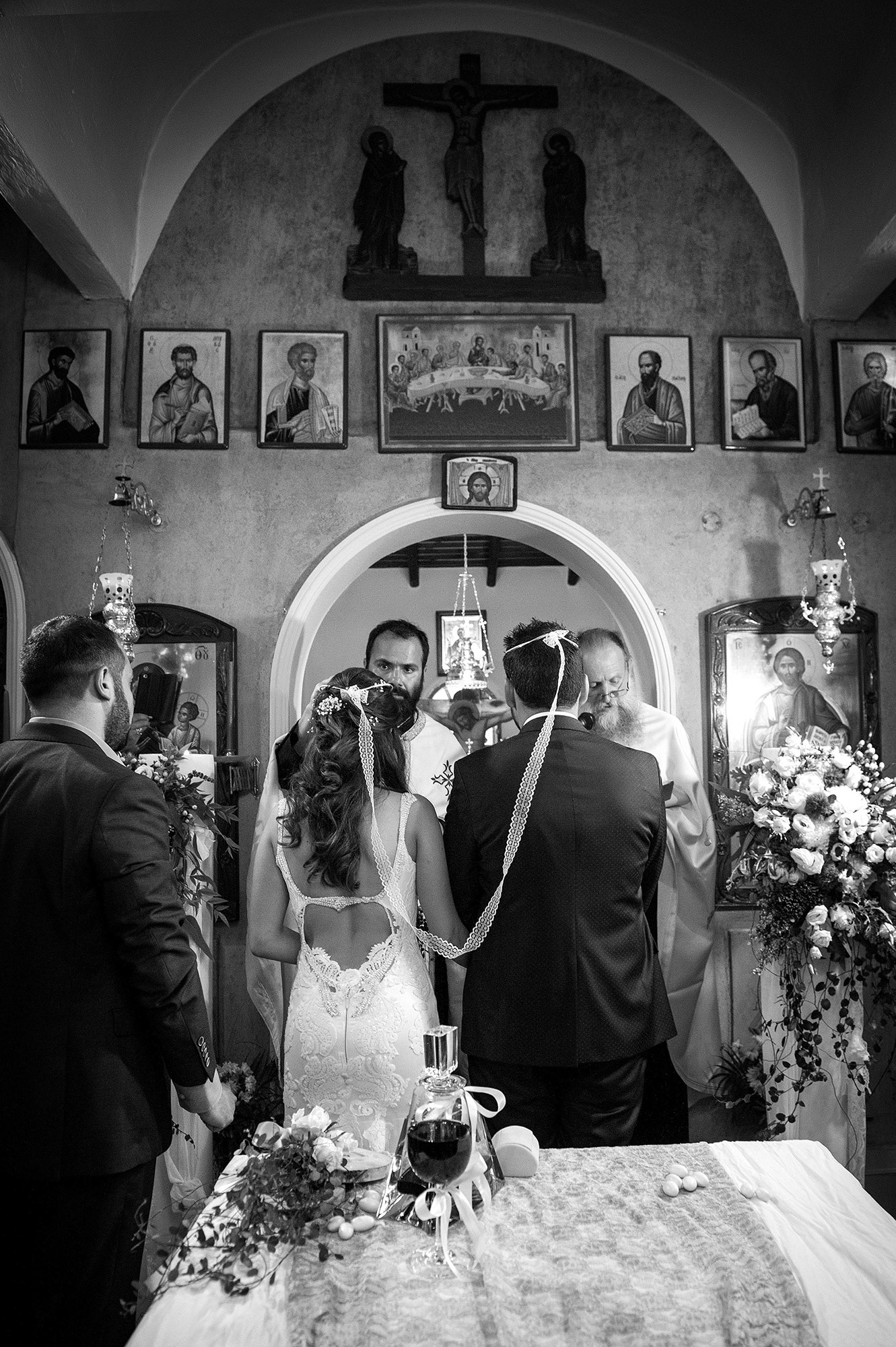 Ο ιερέας τελεί το μυστήριο της στέψης, καθώς η νύφη και ο γαμπρός στέκονται μπροστά στο ιερό δεμένοι με τα στέφανα.   The priest performs the Orthodox wedding crowning ceremony as the bride and groom stand before the altar joined by their crowns.