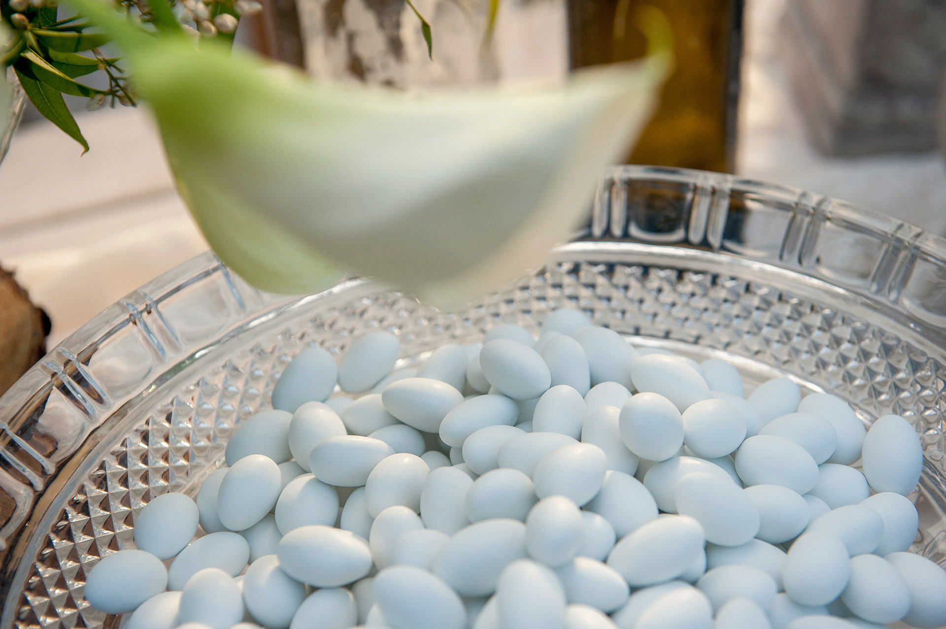 Κουφέτα σε γυάλινη πιατέλα, λεπτομέρεια από τον στολισμό τραπεζιού γάμου με λουλούδια και πρασινάδες.     Sugared almonds in a glass dish, detail from a wedding table decorated with flowers and greenery.