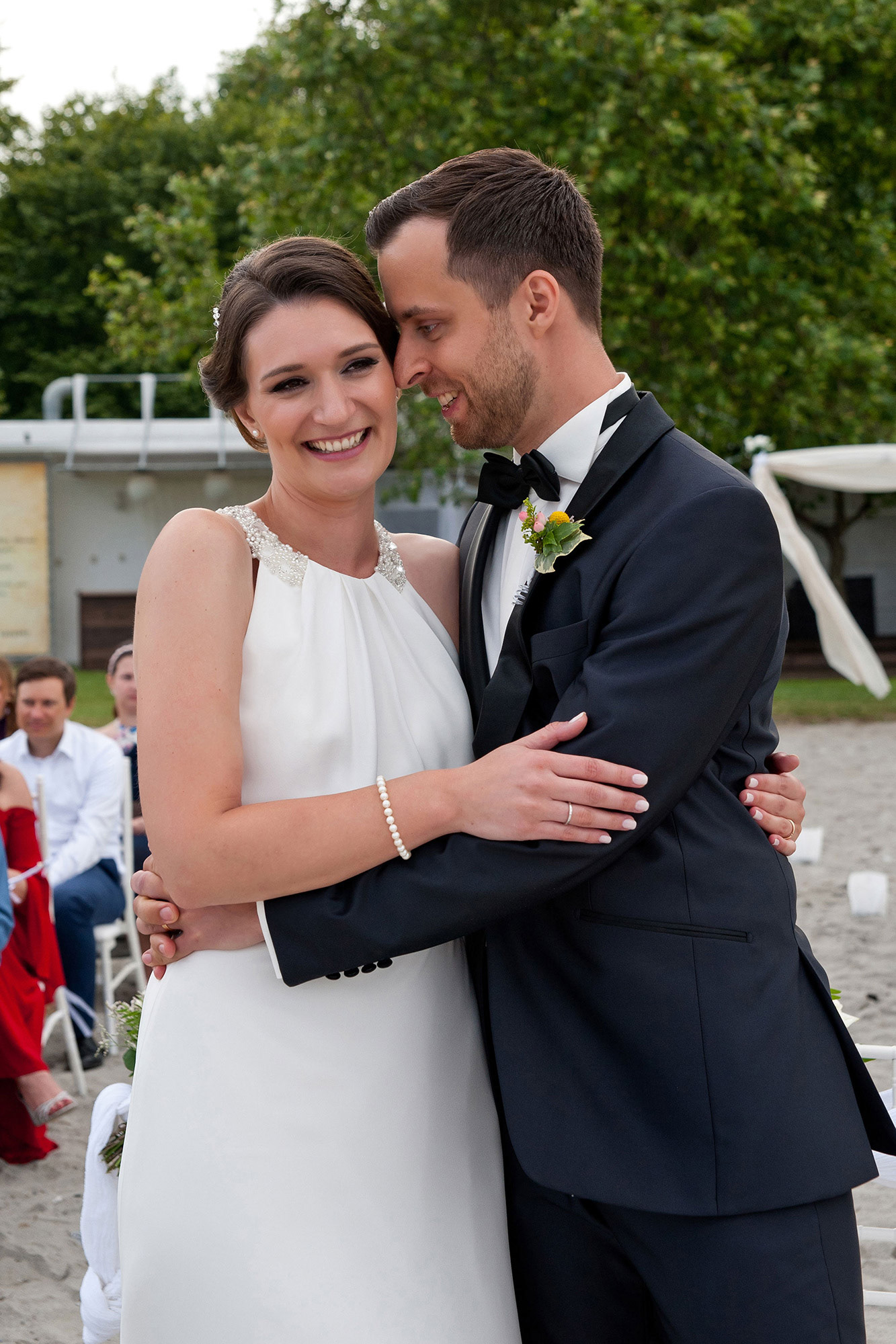 Οι νεόνυμφοι αγκαλιάζονται χαμογελαστοί μετά το φιλί στην παραλία   The newlyweds embrace happily after the kiss on the beach