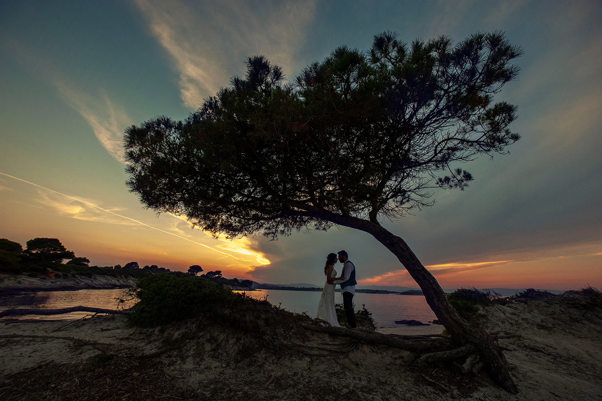 Σιλουέτα του ζευγαριού κάτω από ένα δέντρο στο ηλιοβασίλεμα, στη Σάρτη Χαλκιδικής, με φόντο τον ουρανό και τη θάλασσα. Silhouette of the couple under a tree at sunset in Sarti, Halkidiki, with the sky and sea in the background.
